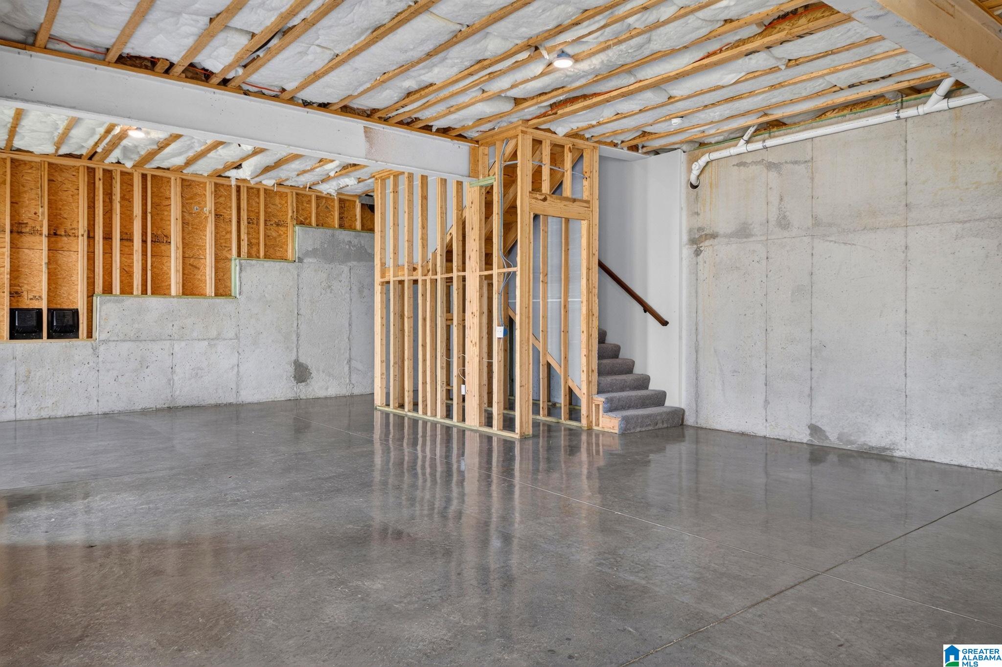 Unfinished basement with exposed framing, concrete floors, and stairs.