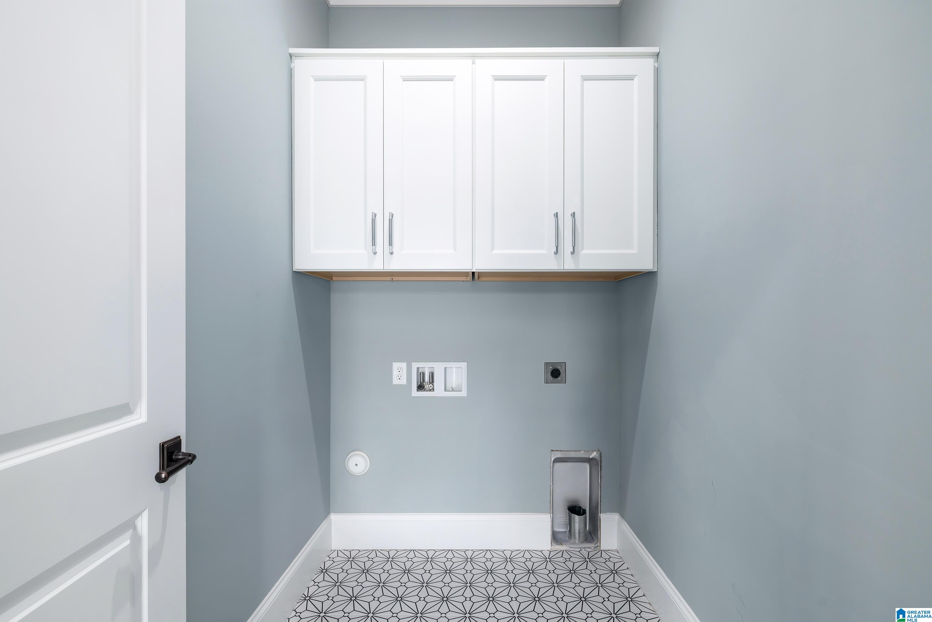 Empty laundry room with white cabinets, appliance hookups, and geometric patterned tile flooring.
