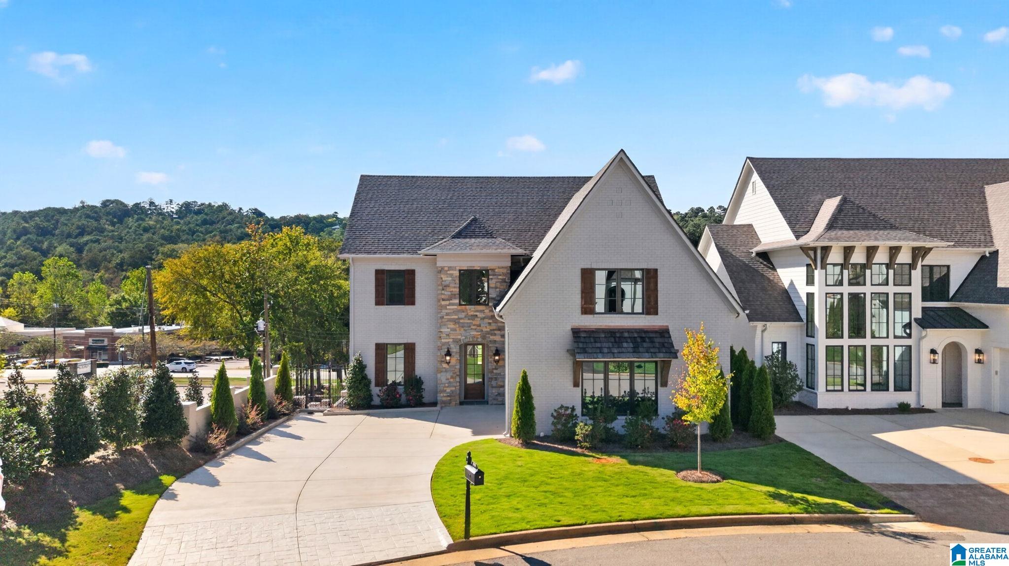 Large white-brick house with stone accents, tall windows, landscaped lawn, and curved driveway.