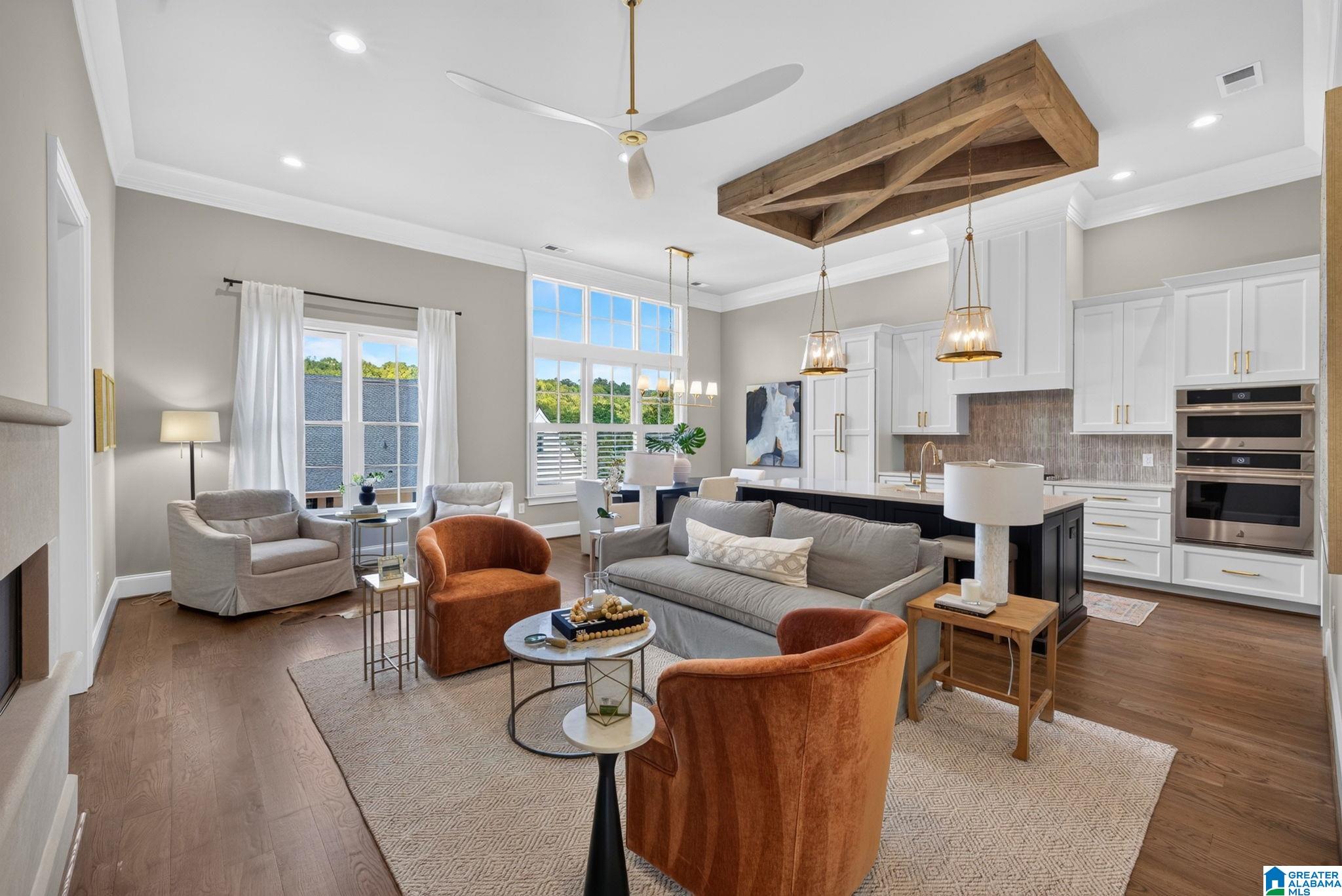 Open-plan living room and kitchen with rust-colored armchairs and a large exposed wood ceiling beam.