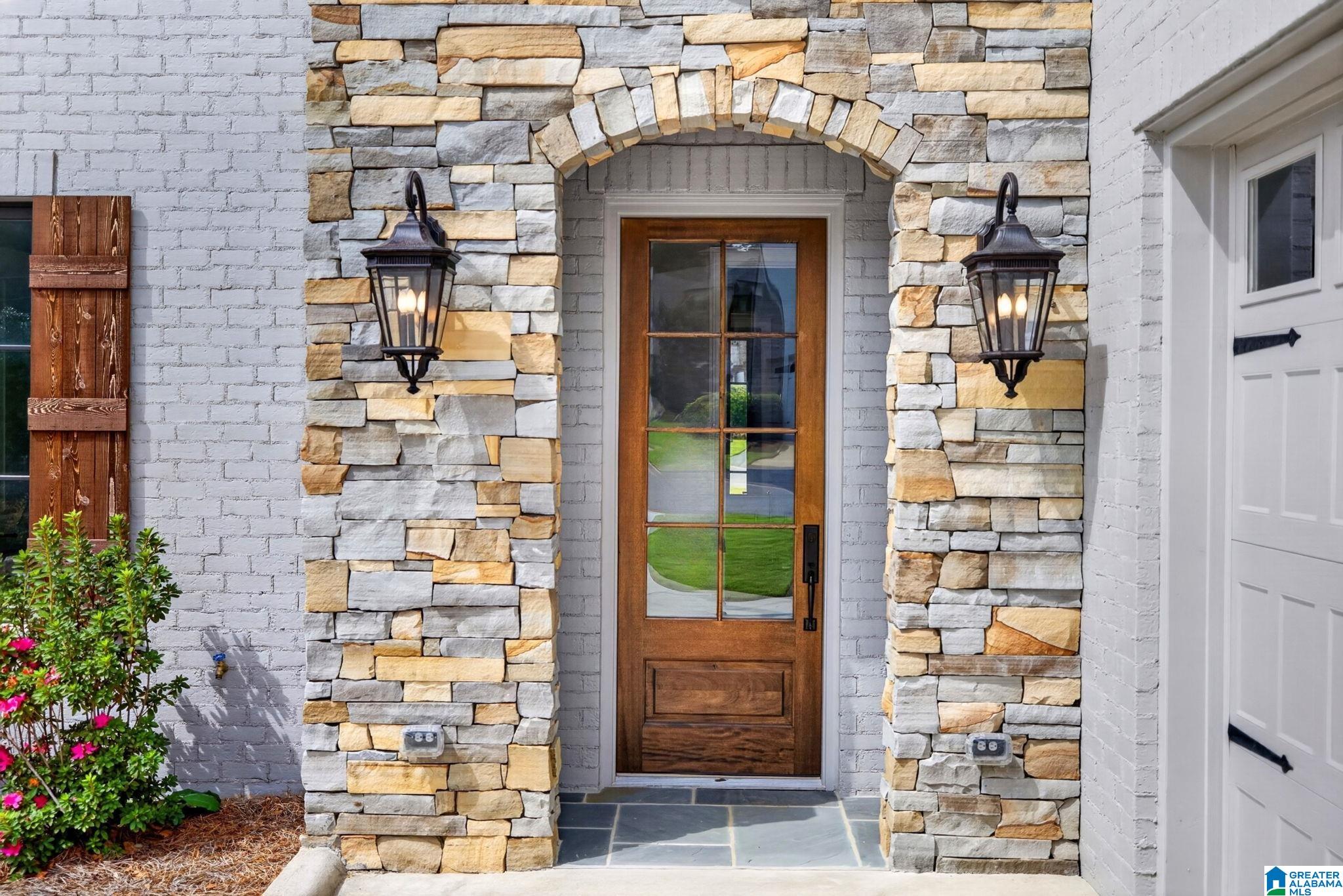 Stone-arched front entry with a glass-paneled wooden door and matching lanterns.