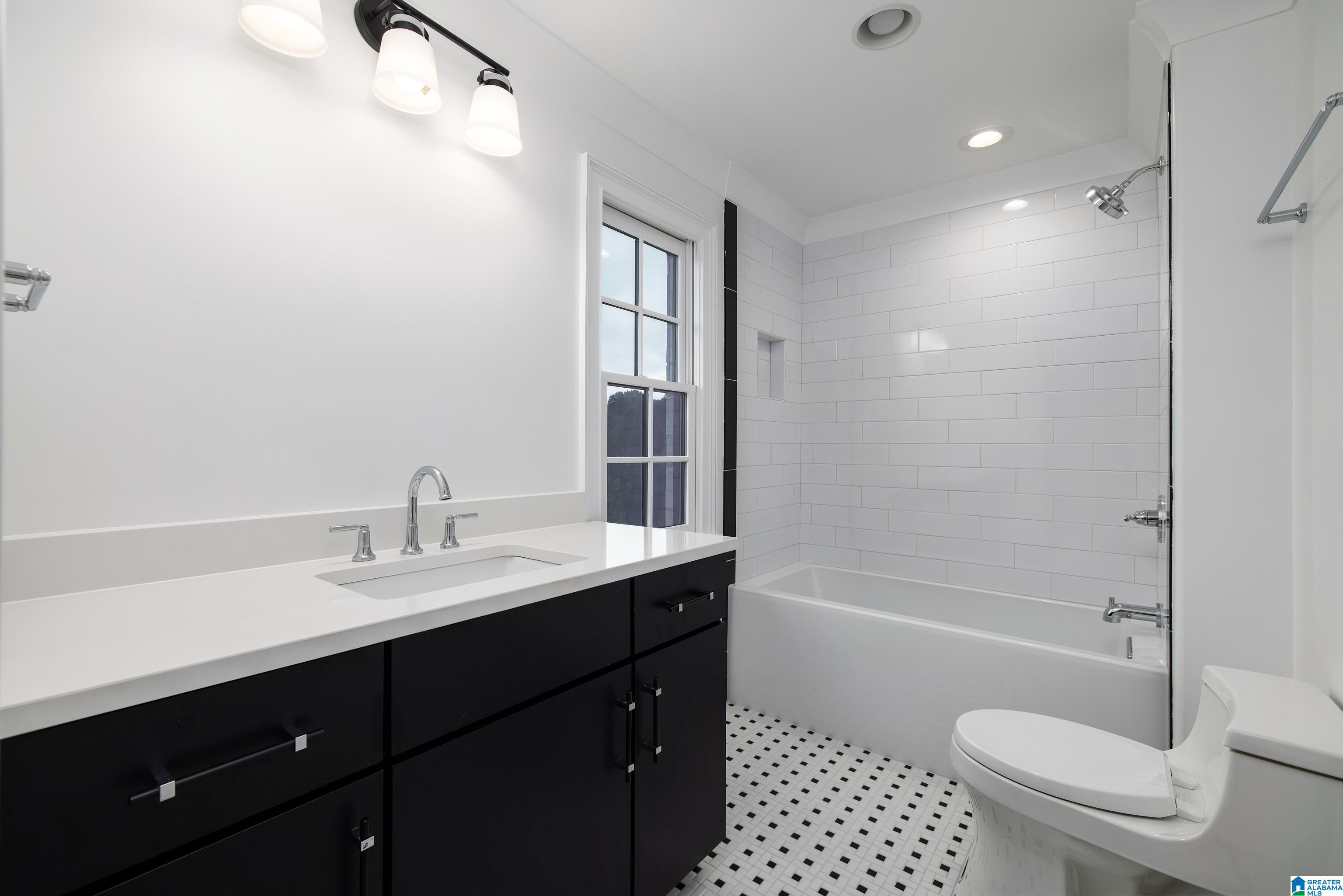 Bathroom with a black vanity, white subway-tile tub surround, and black-and-white mosaic floor.