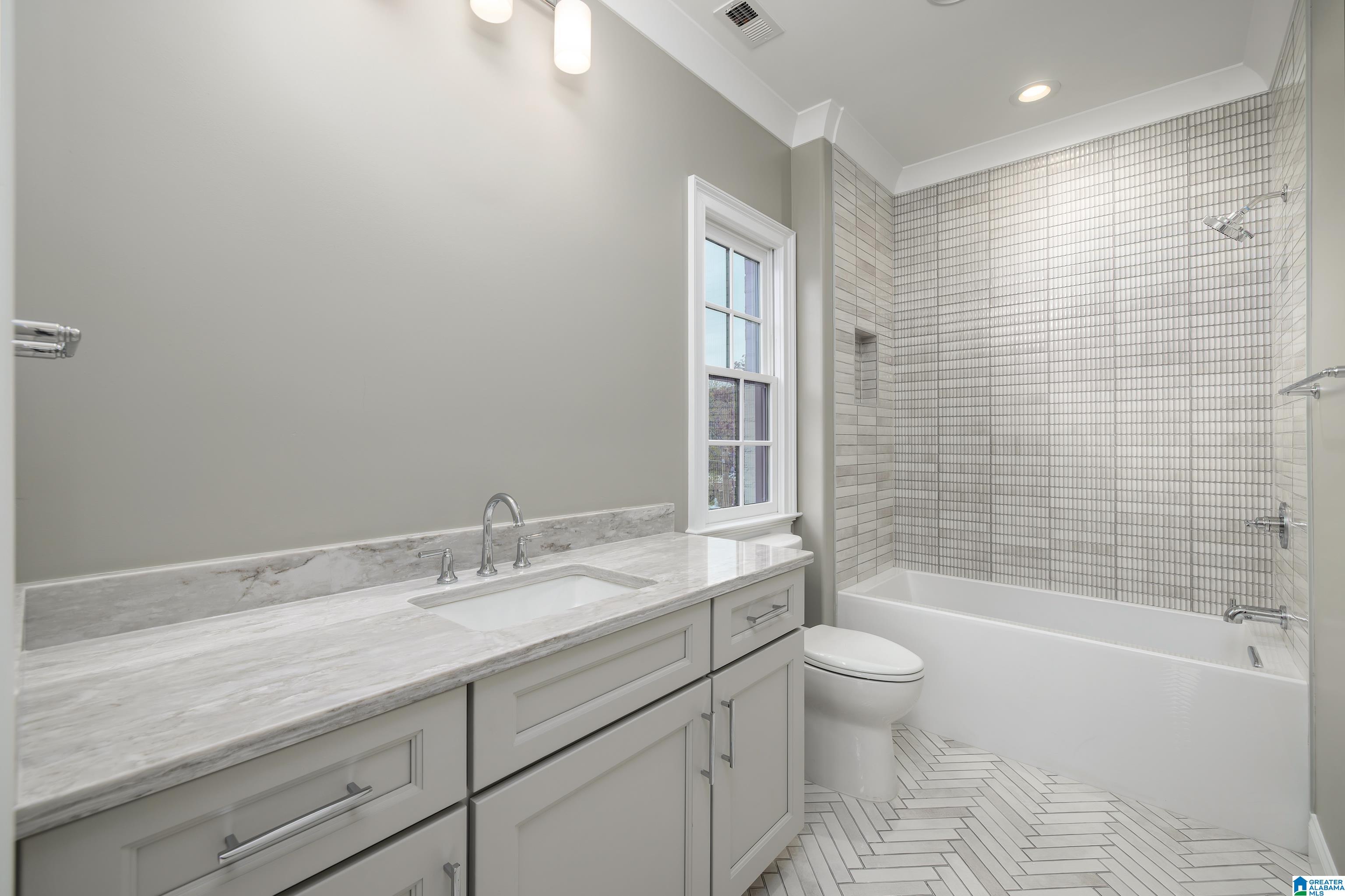 Bathroom with a marble-look vanity, gray tiled tub surround, and white herringbone floor.