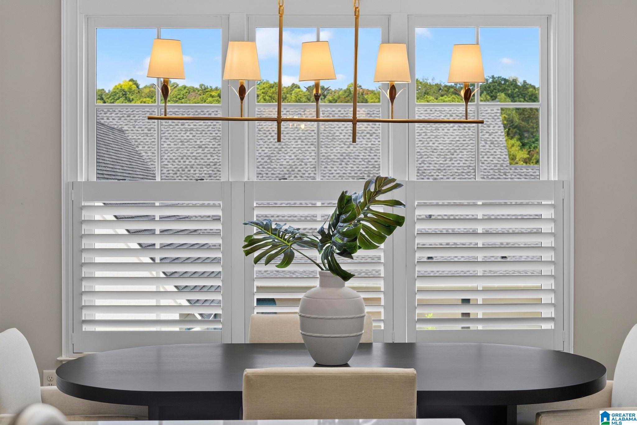 Dining room with a dark oval table, brass chandelier, and large shuttered windows.