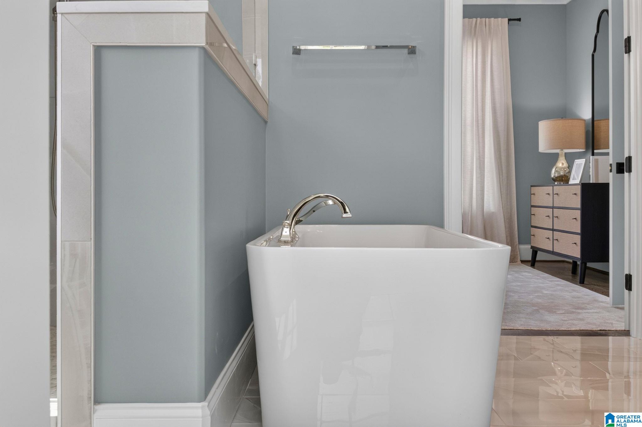 Bathroom with a freestanding white tub, chrome faucet, and glass shower partition.