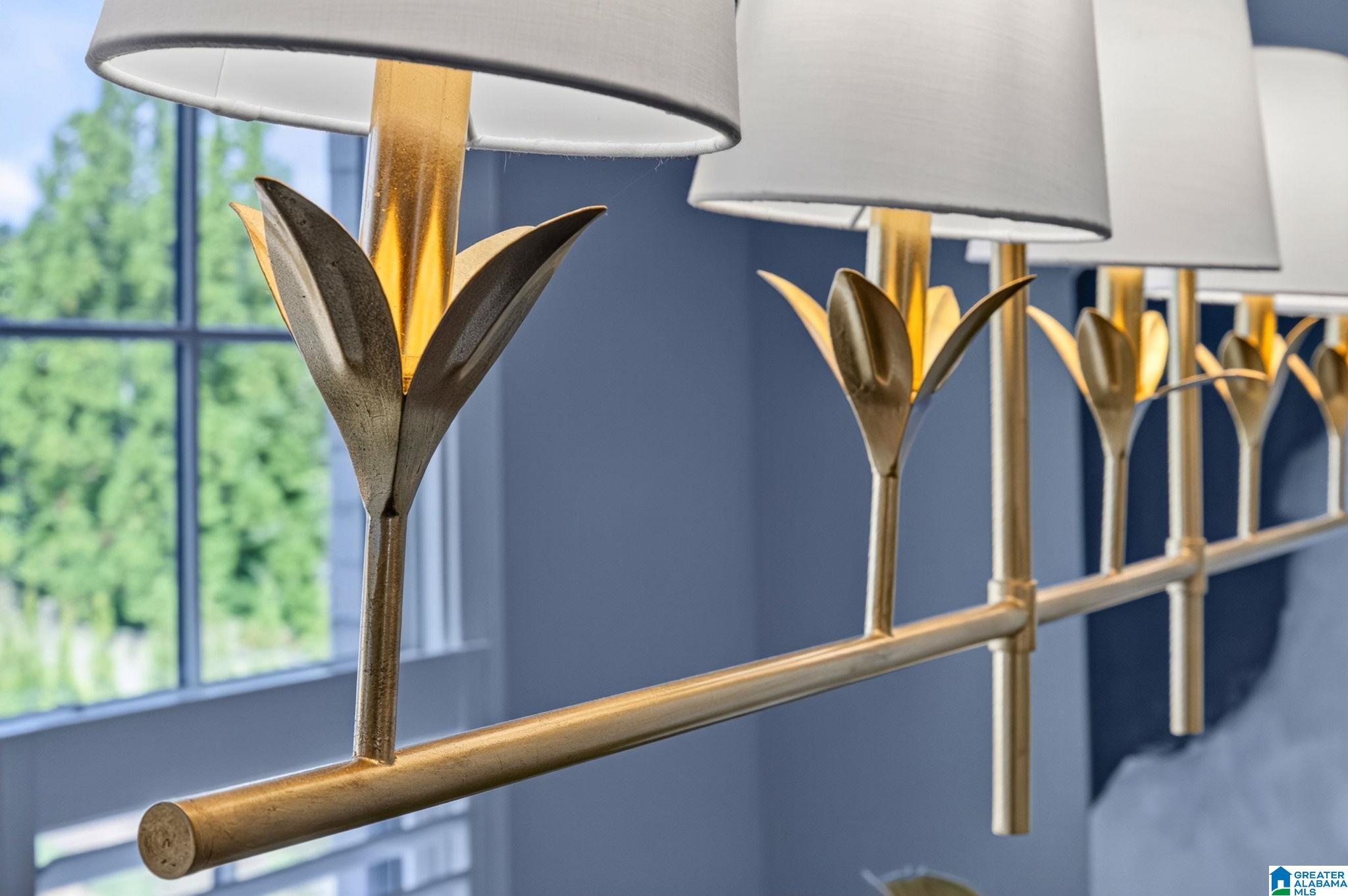 Brass bedroom light fixture with sculptural metal details and white shades above a bed.