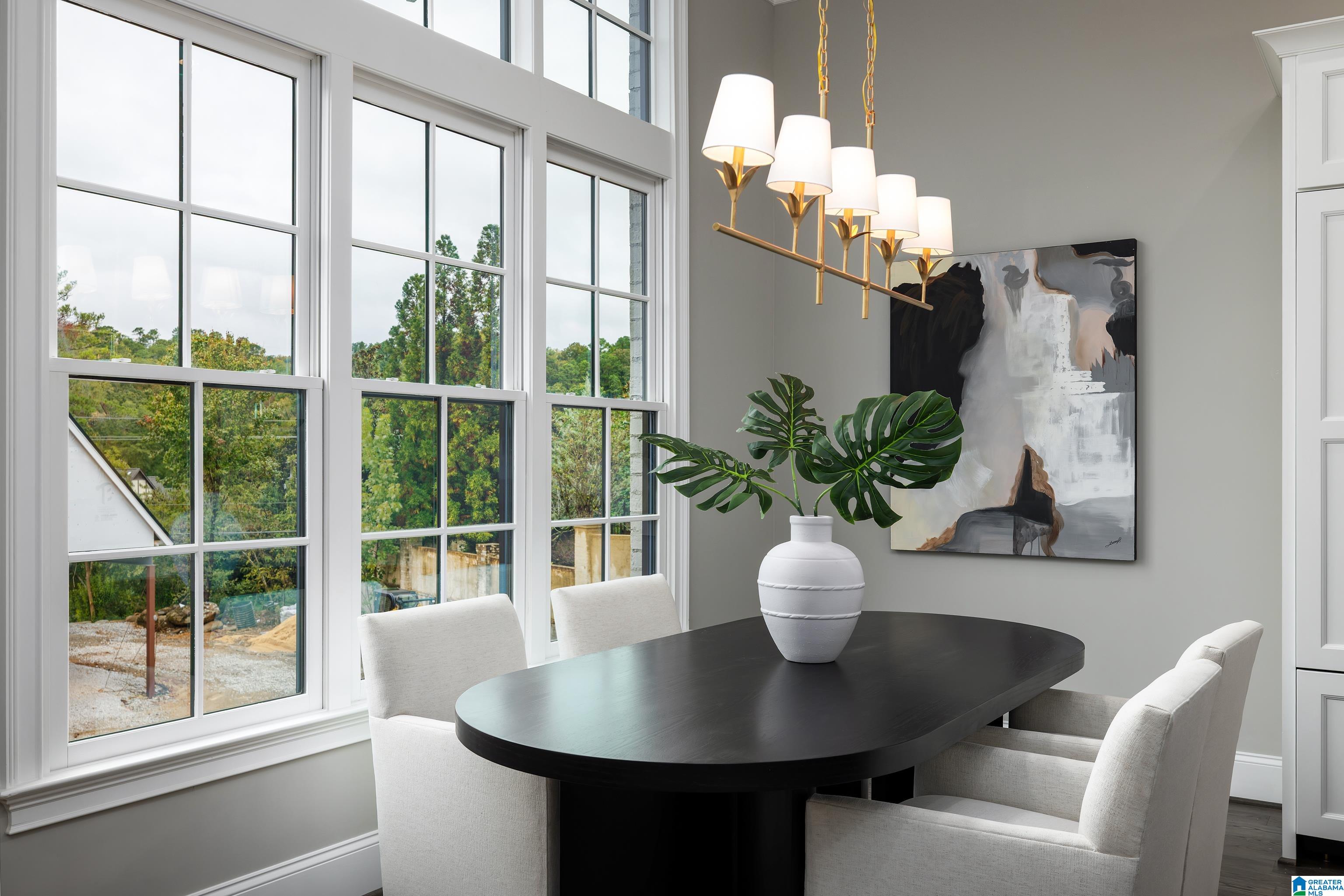 Dining room with a black oval table, white chairs, and tall windows overlooking trees.