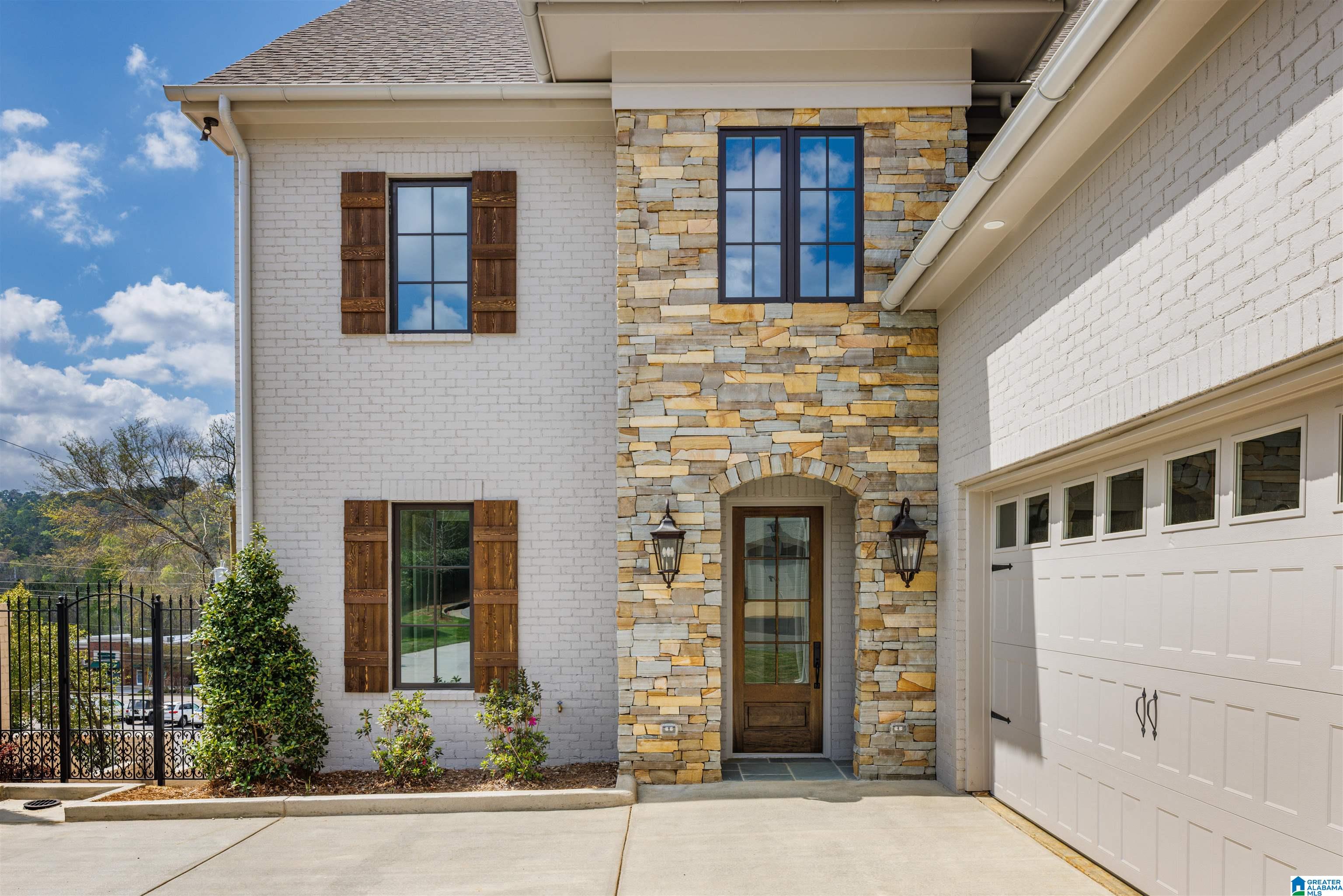 Home entrance with a stone facade, arched doorway, dark wood shutters, and an attached garage.