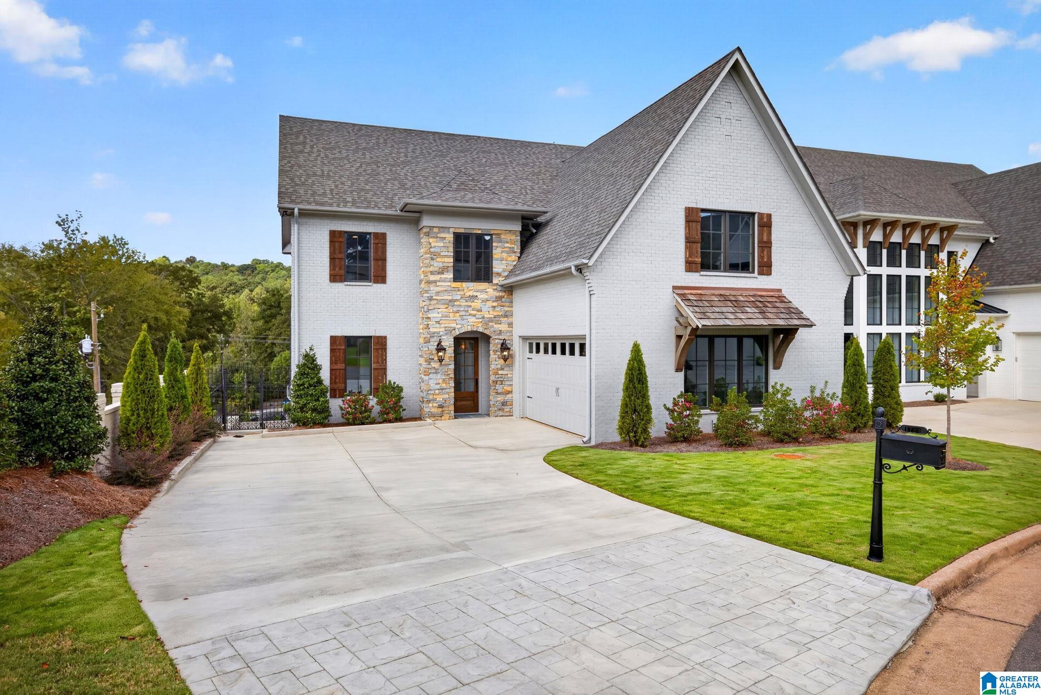 White brick house with stone entry, steep gables, wood shutters, and a wide paved driveway.