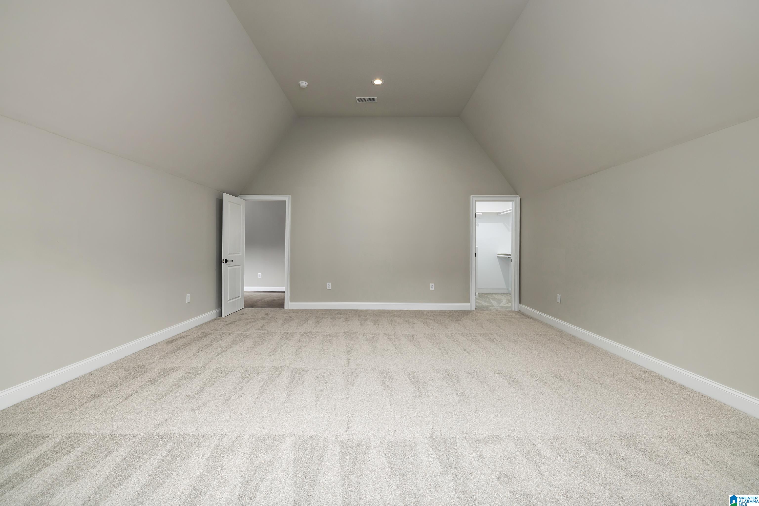 Empty carpeted room with a high sloped ceiling and two doorways.