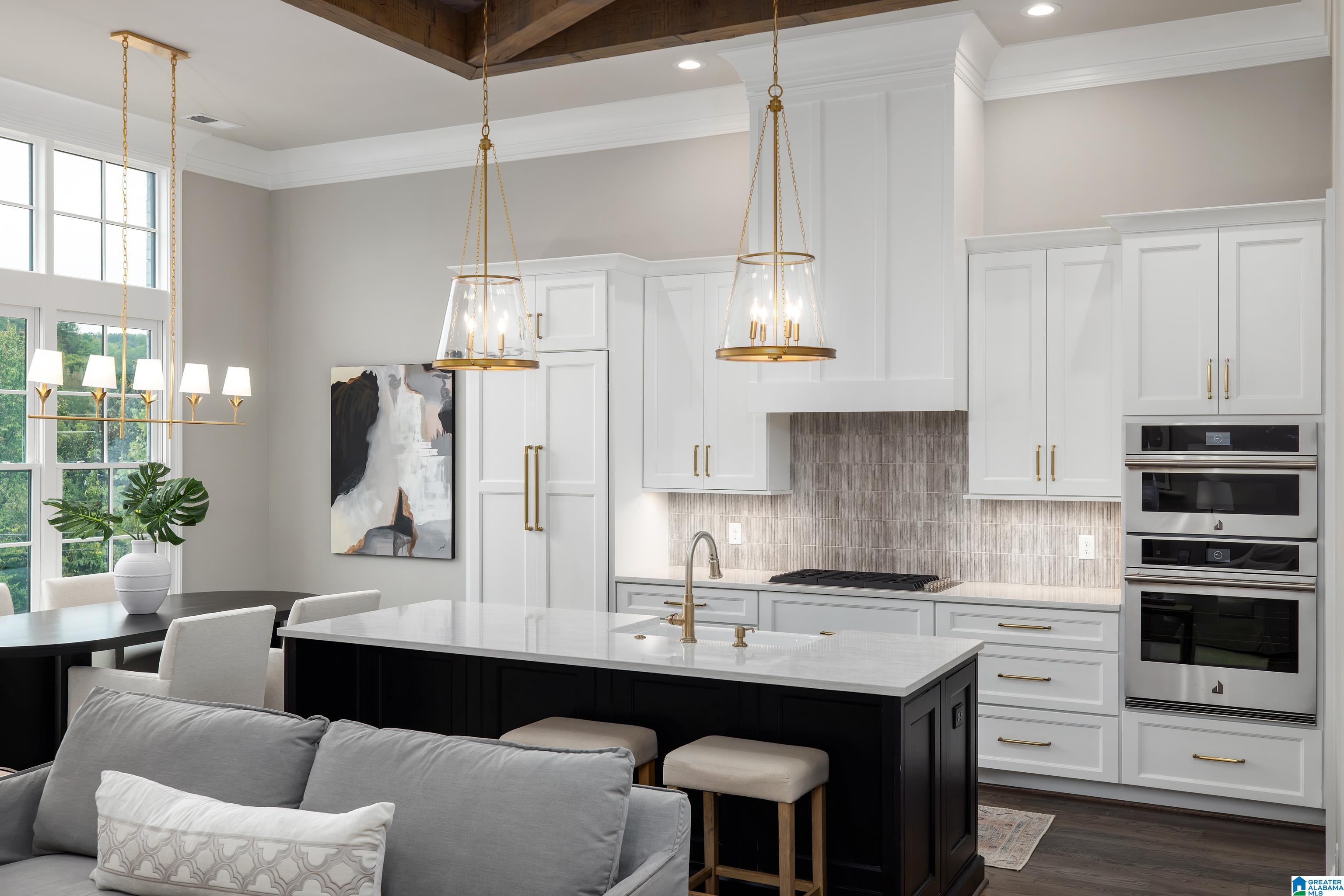 Open-plan kitchen with white cabinets, a dark island, brass pendants, and tall windows.