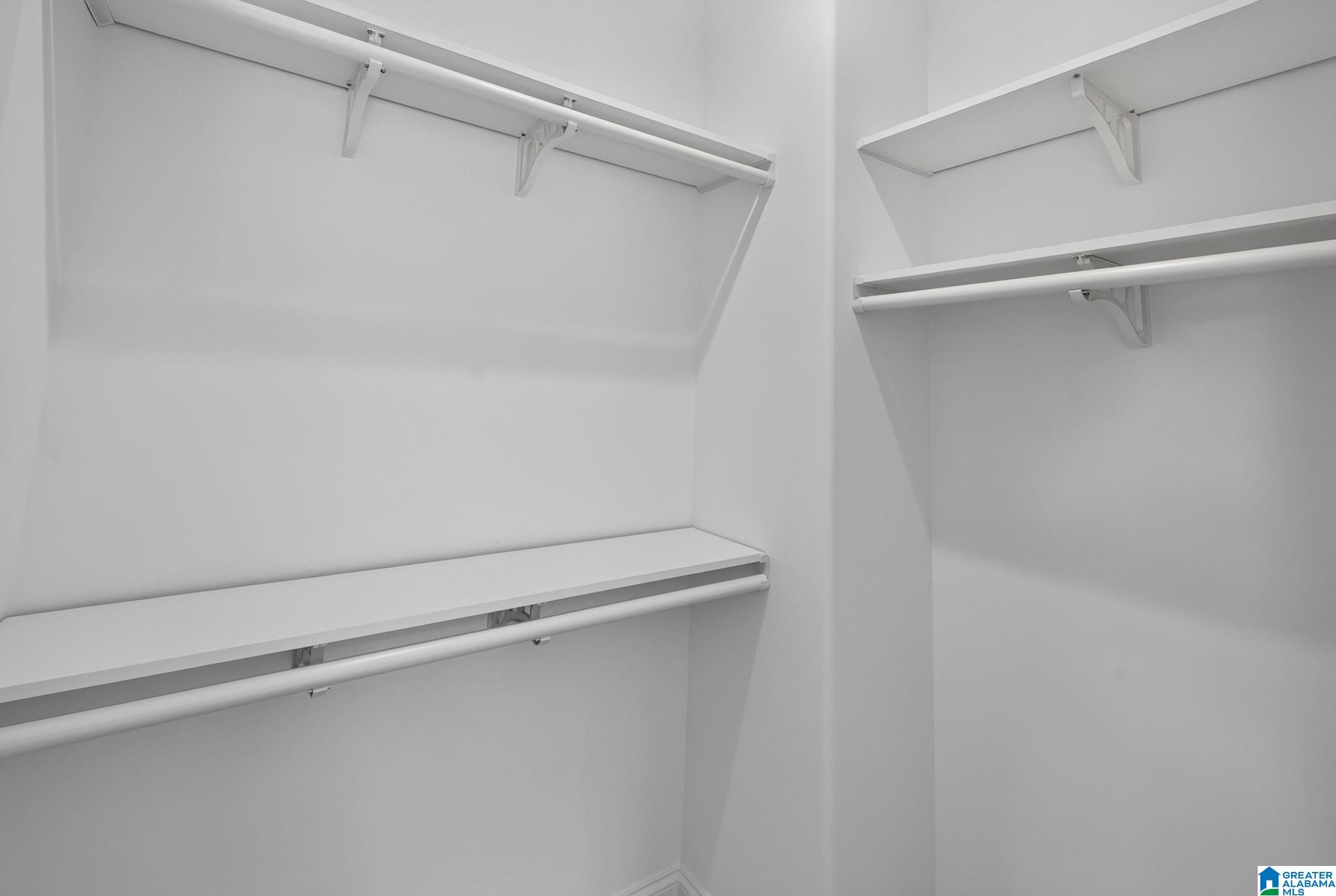 Empty walk-in closet with white built-in shelves and hanging rods on two walls.