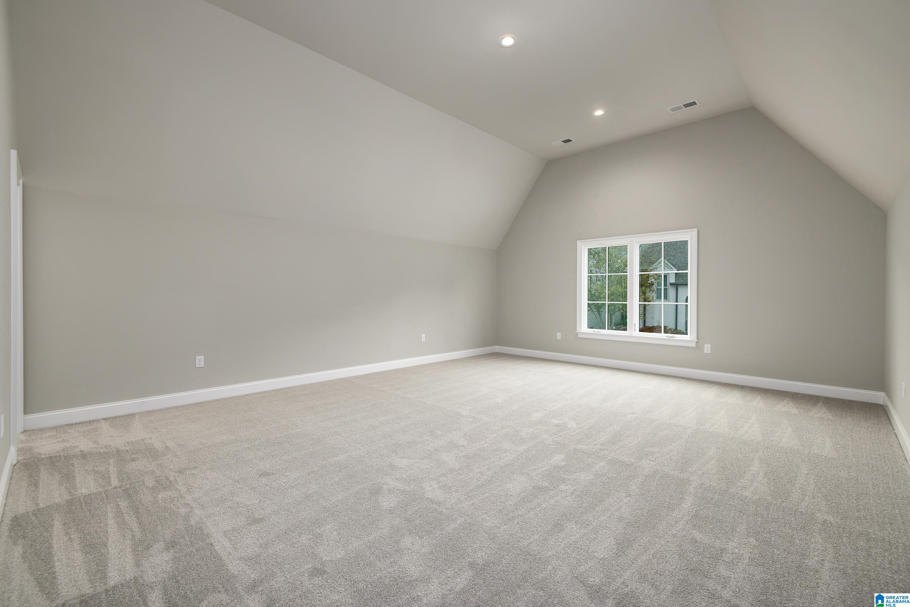 Vacant carpeted room with a high sloped ceiling and a large window.