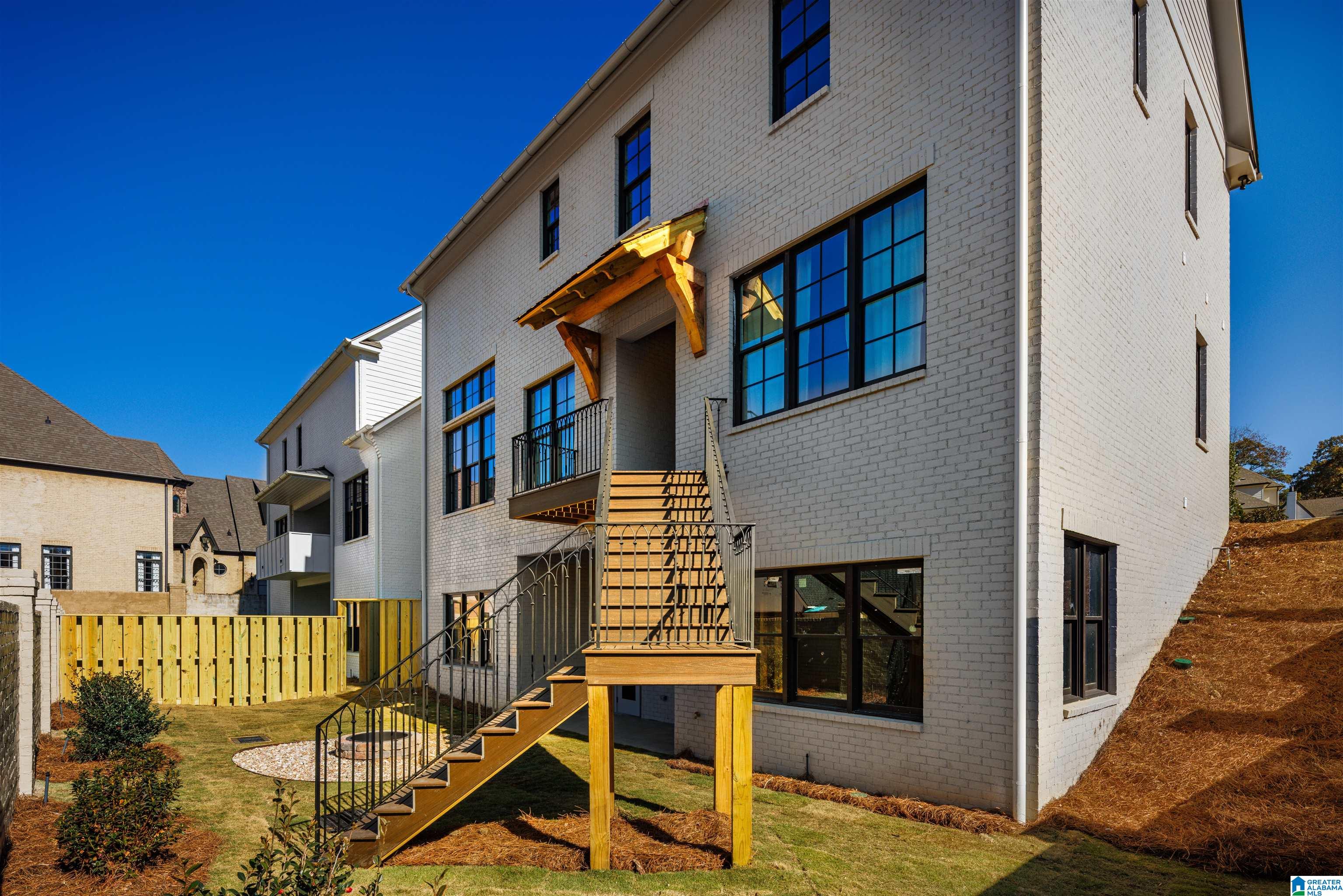 Light brick home with a raised wooden deck and stairs leading to the backyard.