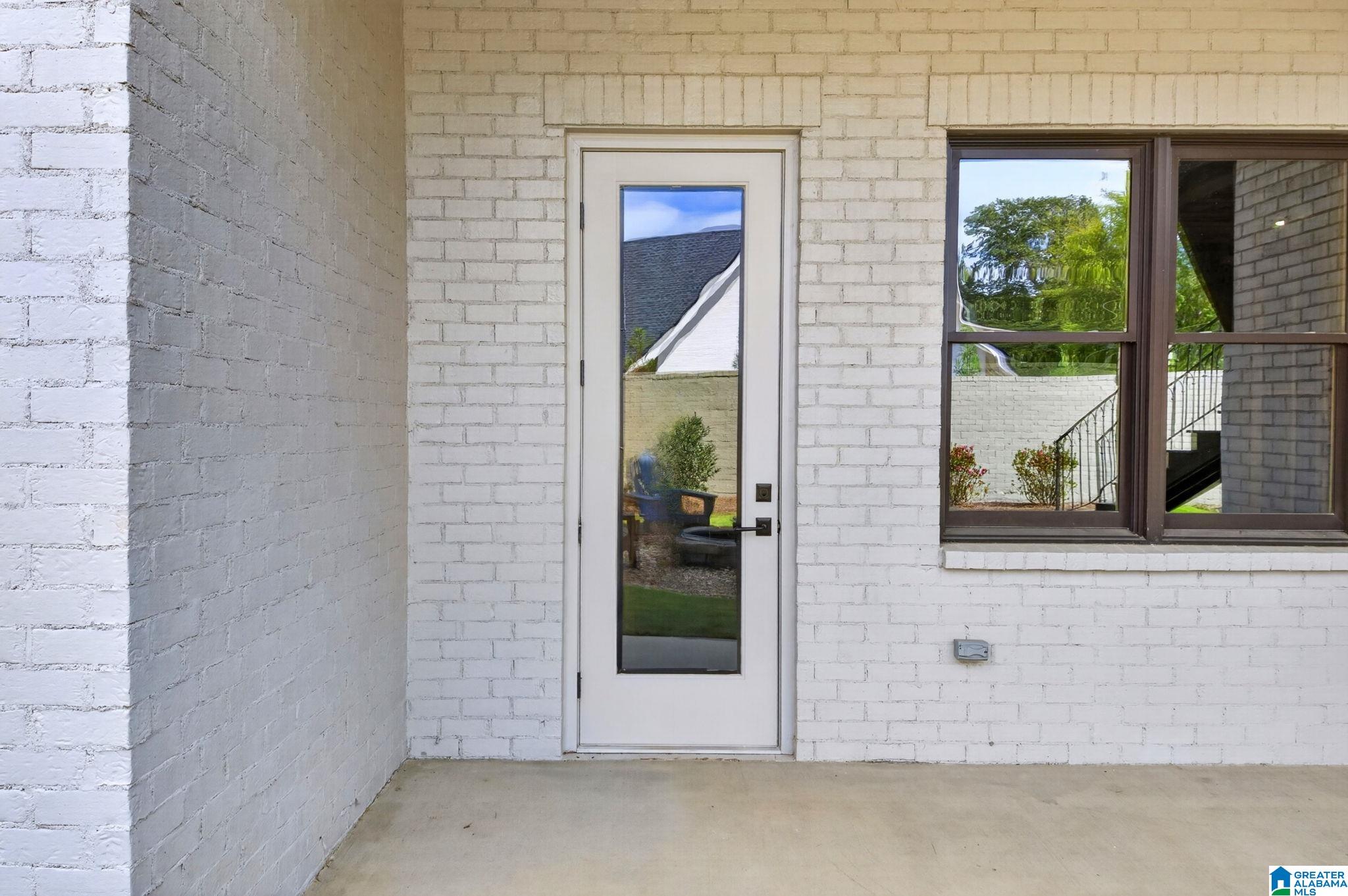 White brick covered entry with a full-length glass door and large dark-framed window.