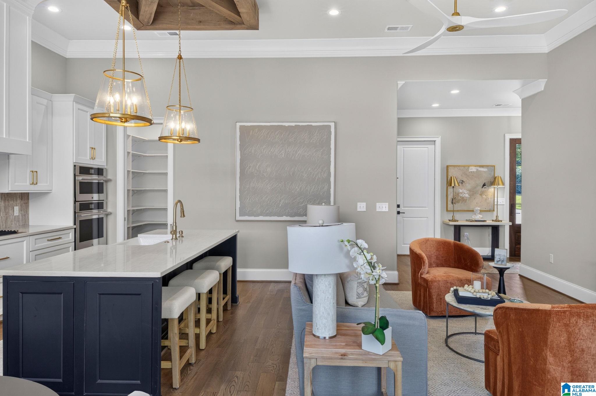 Open-plan kitchen and living room with a navy island, brass pendants, and rust-colored chairs.