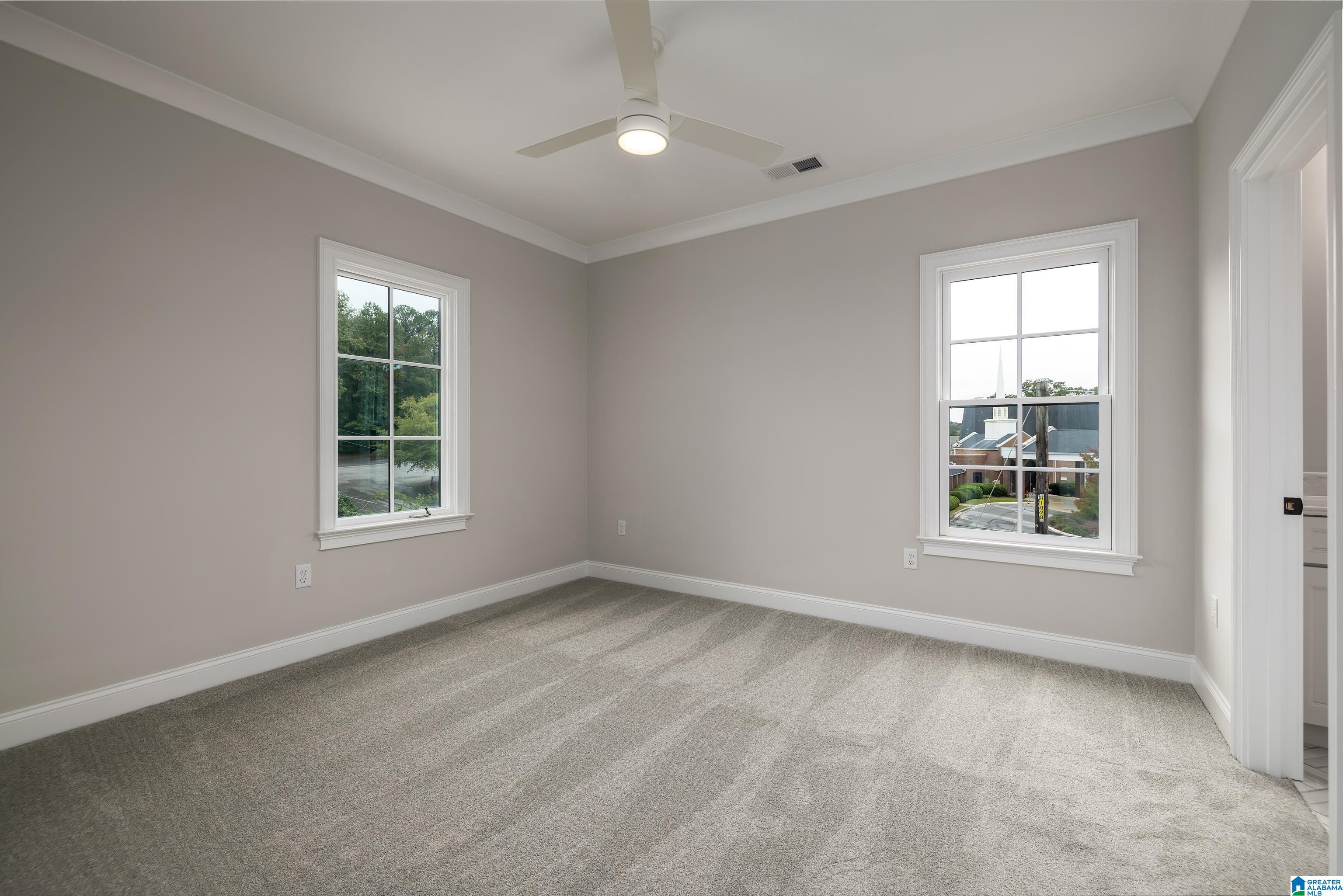 Empty carpeted bedroom with two windows, a ceiling fan, and an open doorway to an adjoining room.