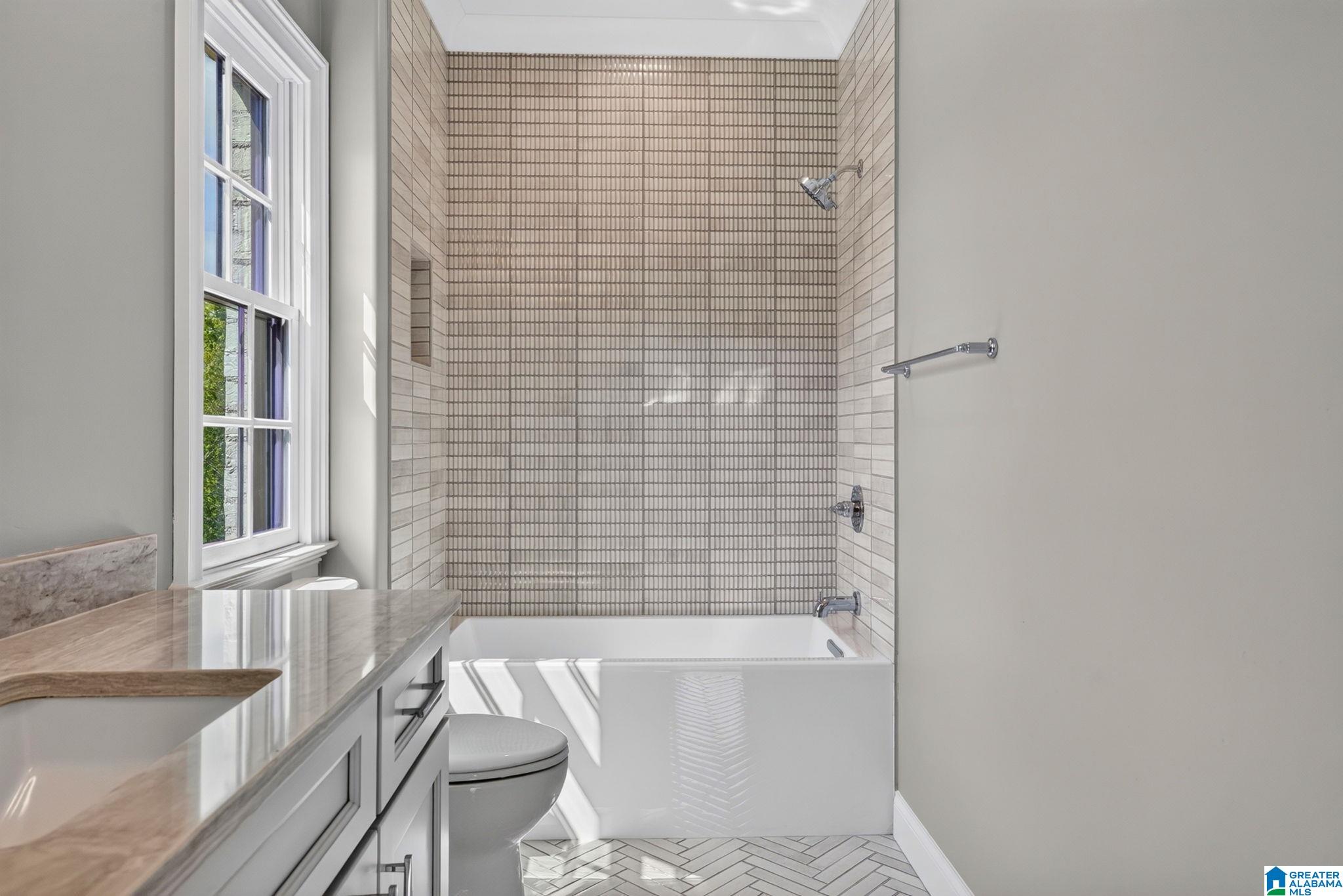 Bathroom with a tiled tub and shower, marble vanity, and large window.