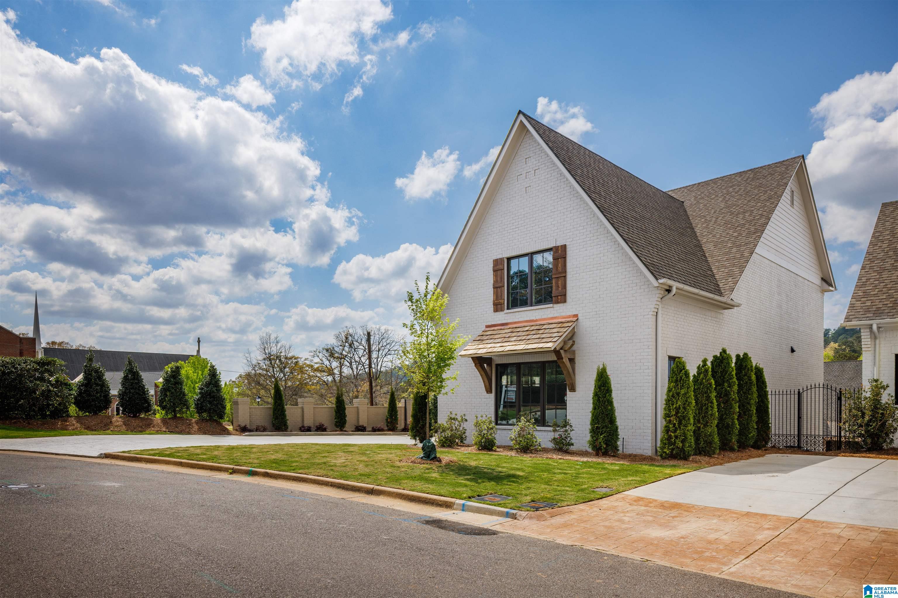 White brick house with steep gabled roofs, a timber entrance awning, and evergreen landscaping.
