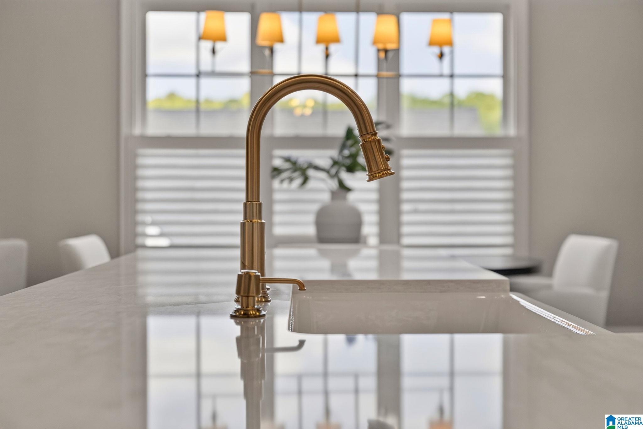 Kitchen island with a brass gooseneck faucet, undermount sink, and large windows behind it.