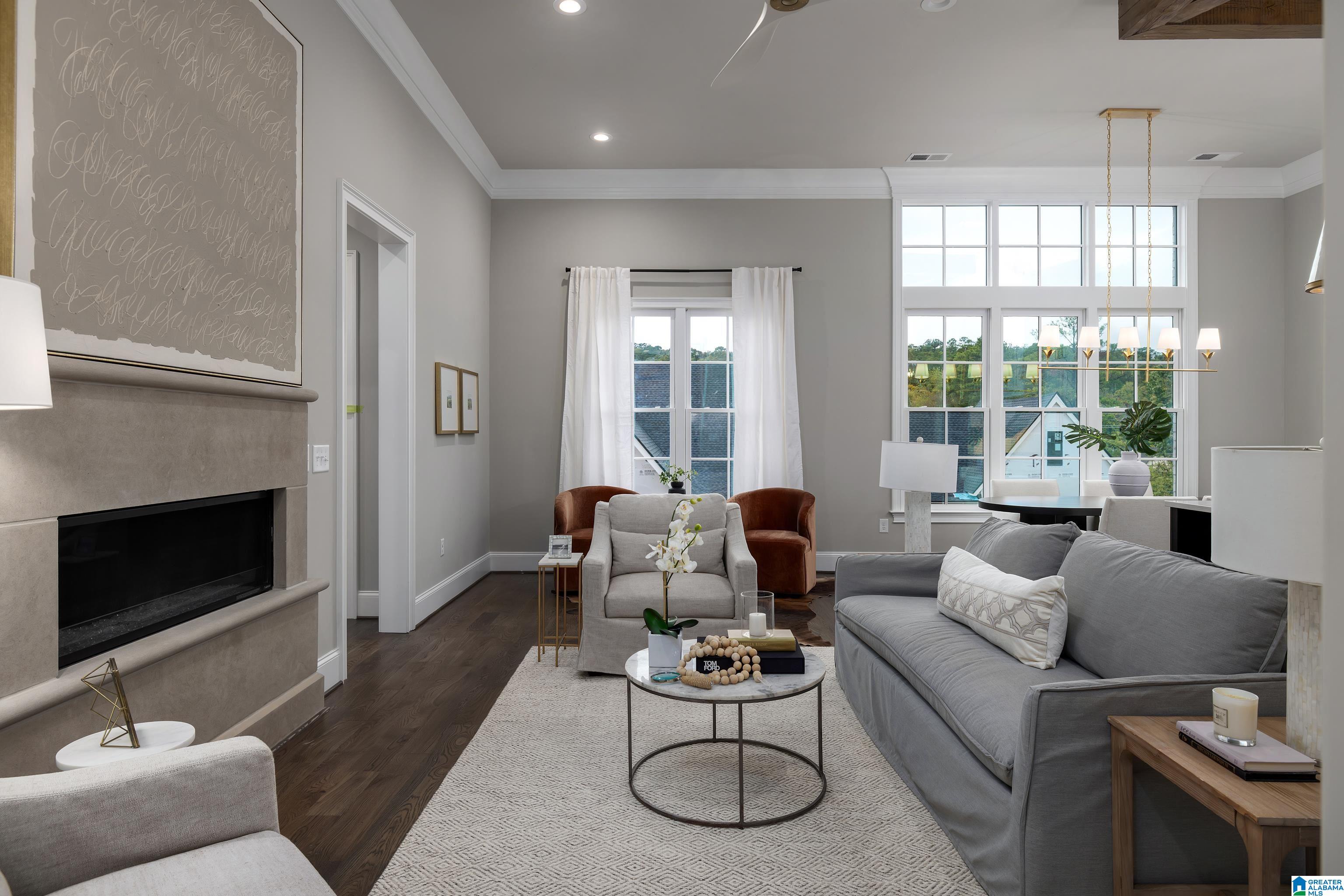 Staged living room with a gray sofa, stone fireplace, and tall windows.