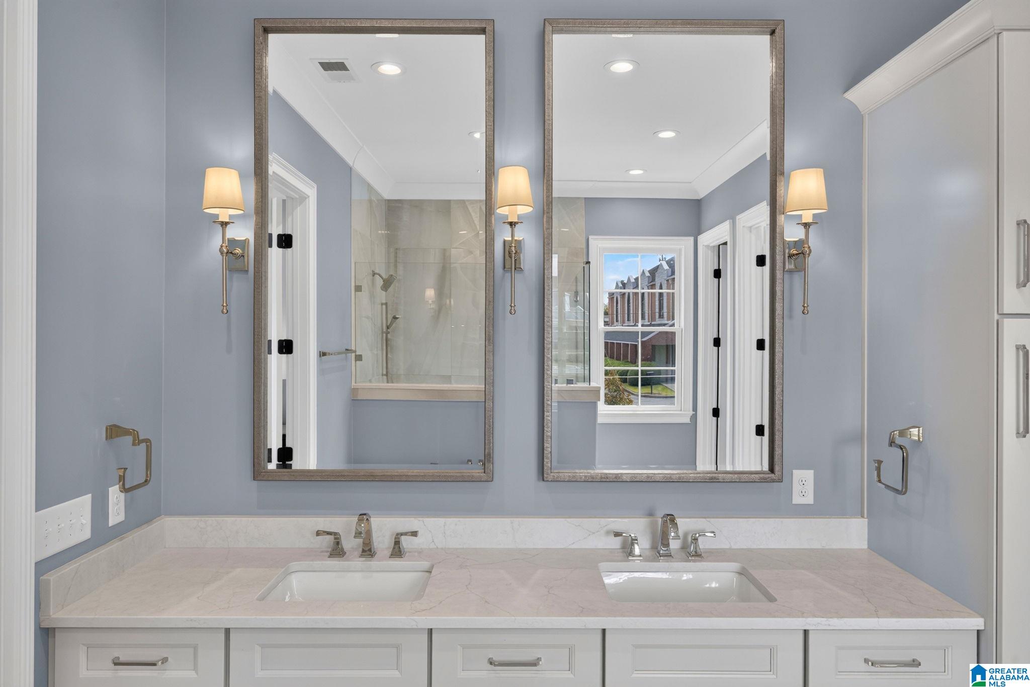 Double-sink bathroom vanity with a marble countertop, framed mirrors, and gray walls.