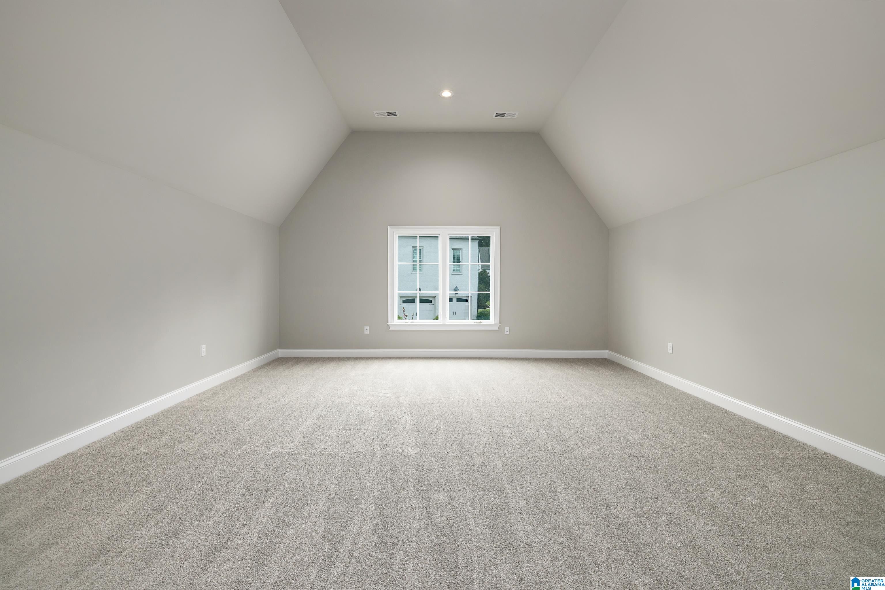 Empty carpeted room with a vaulted ceiling and a centered window.