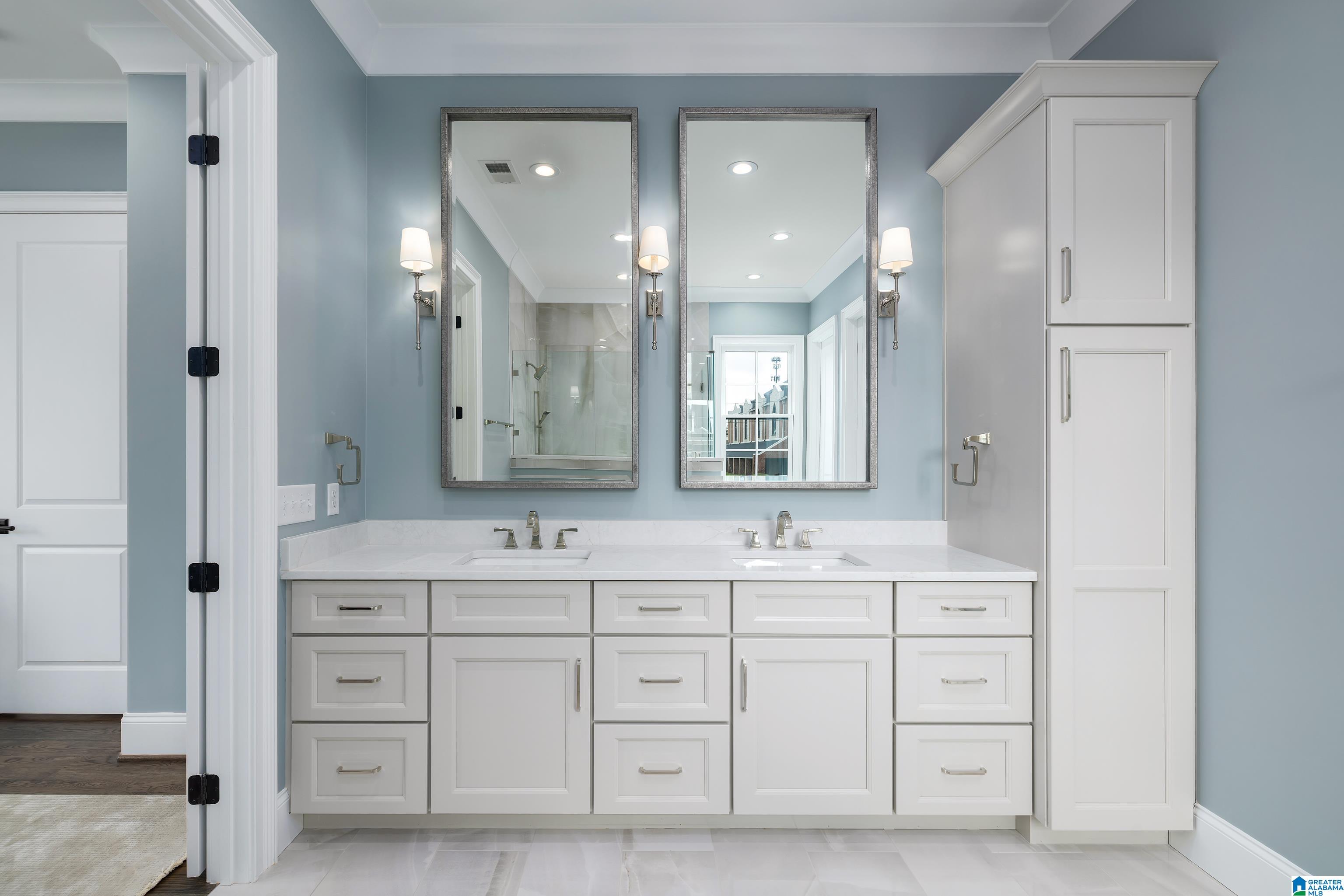 Bathroom with a white double vanity, two framed mirrors and a tall storage cabinet.