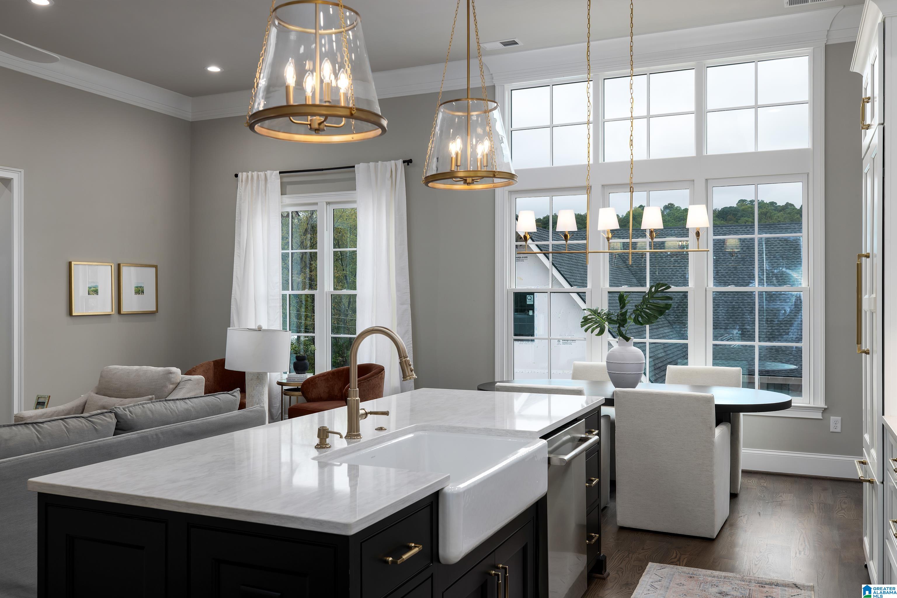 Kitchen with a black island, farmhouse sink, brass fixtures, and tall windows beside the dining area.