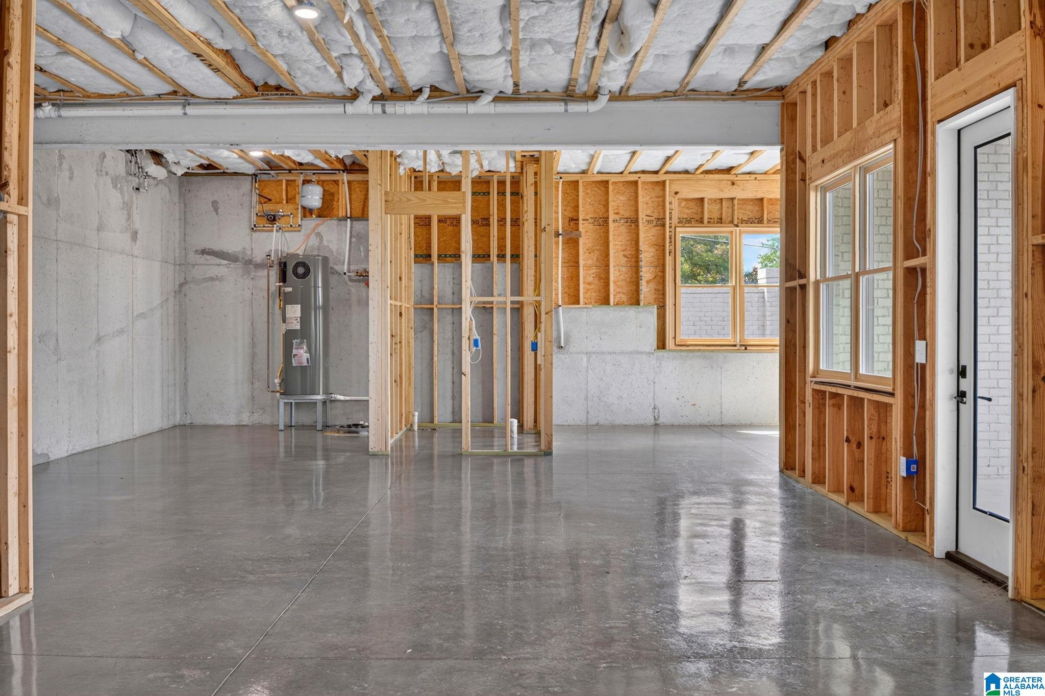 Unfinished interior with exposed framing, a polished concrete floor, utility equipment, windows, and an exterior door.