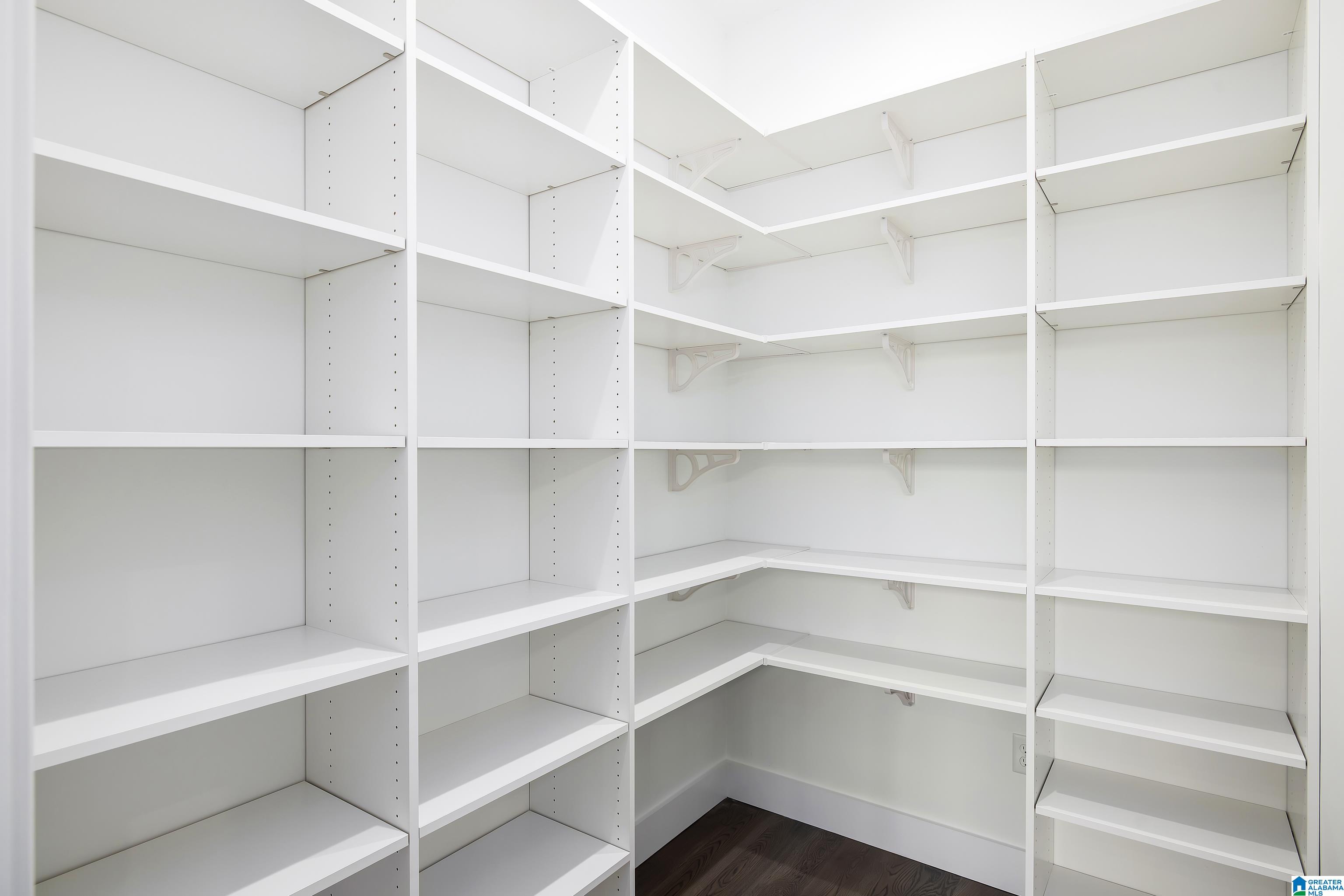 Walk-in pantry with white built-in shelves lining three walls and dark wood flooring.
