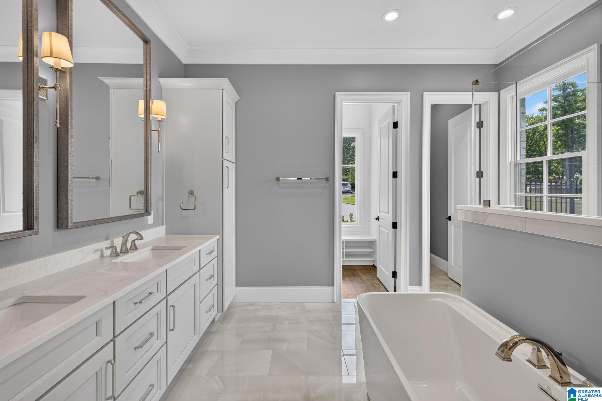 Bathroom with a long double vanity, freestanding tub, and large windows.