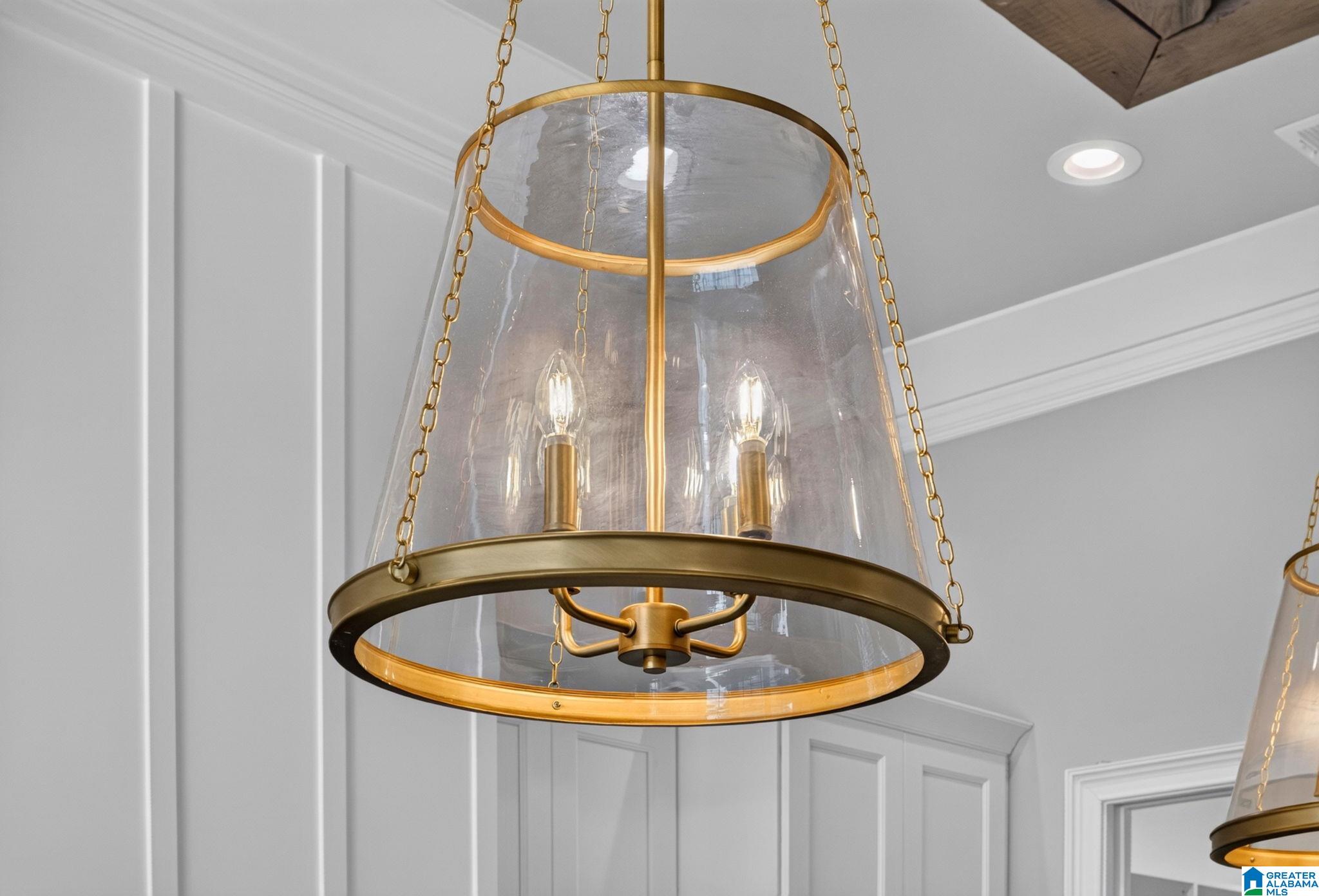 Brass and glass pendant chandelier with chain suspension against white paneled walls.