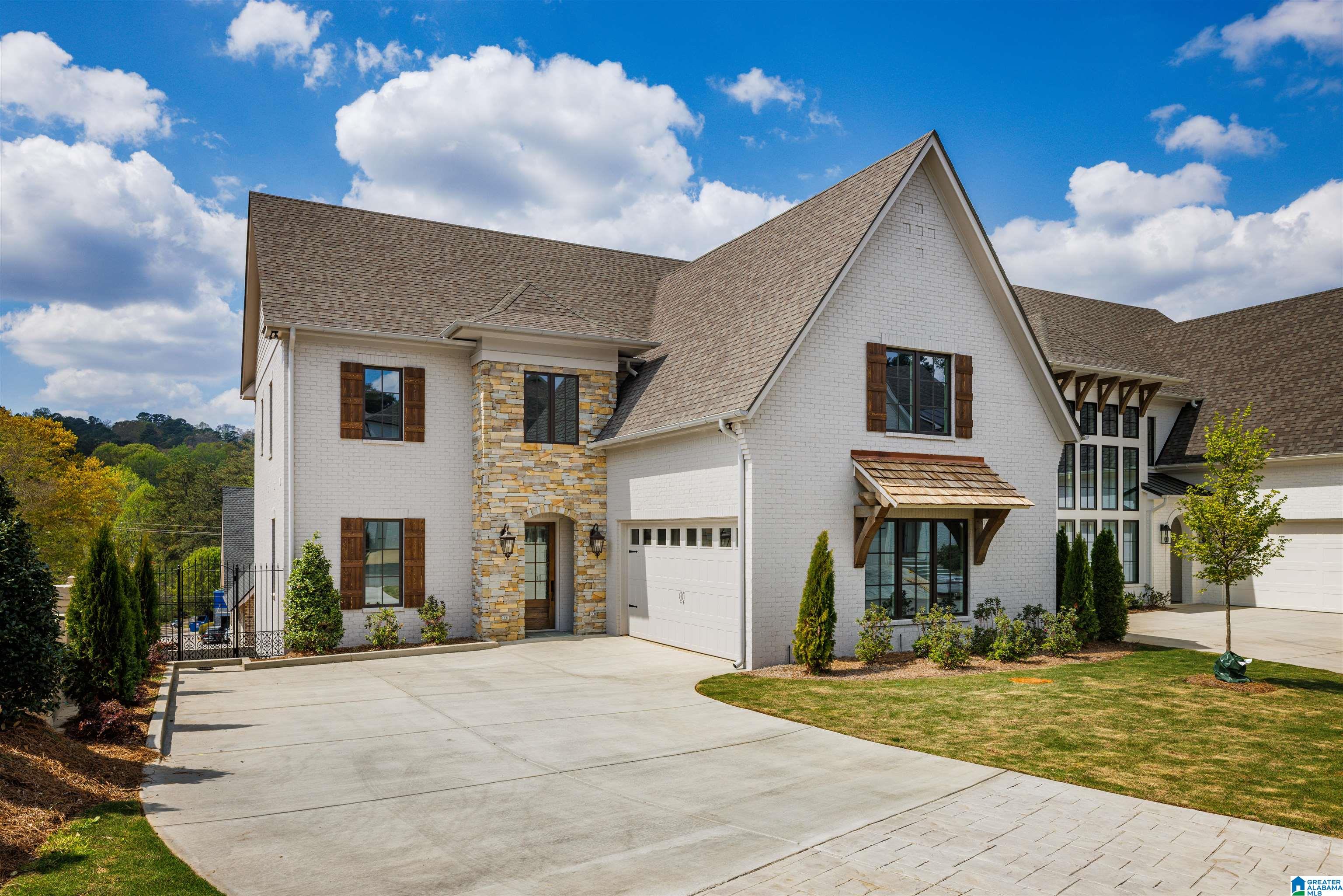White brick house with stone accents, steep roofs, dark shutters, and a broad concrete driveway.