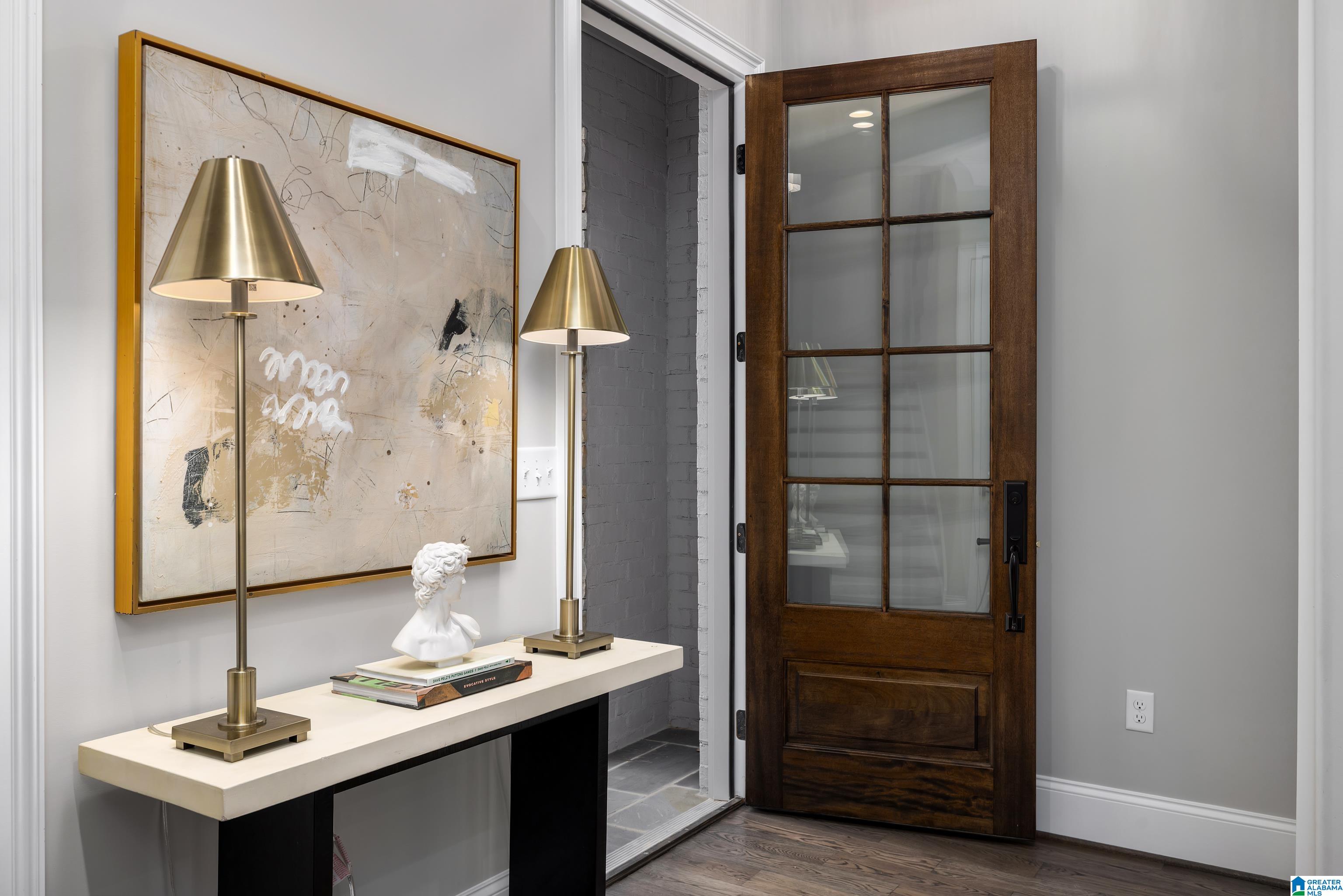 Entryway with an open glass-paneled wood door, brass lamps, and abstract wall art.