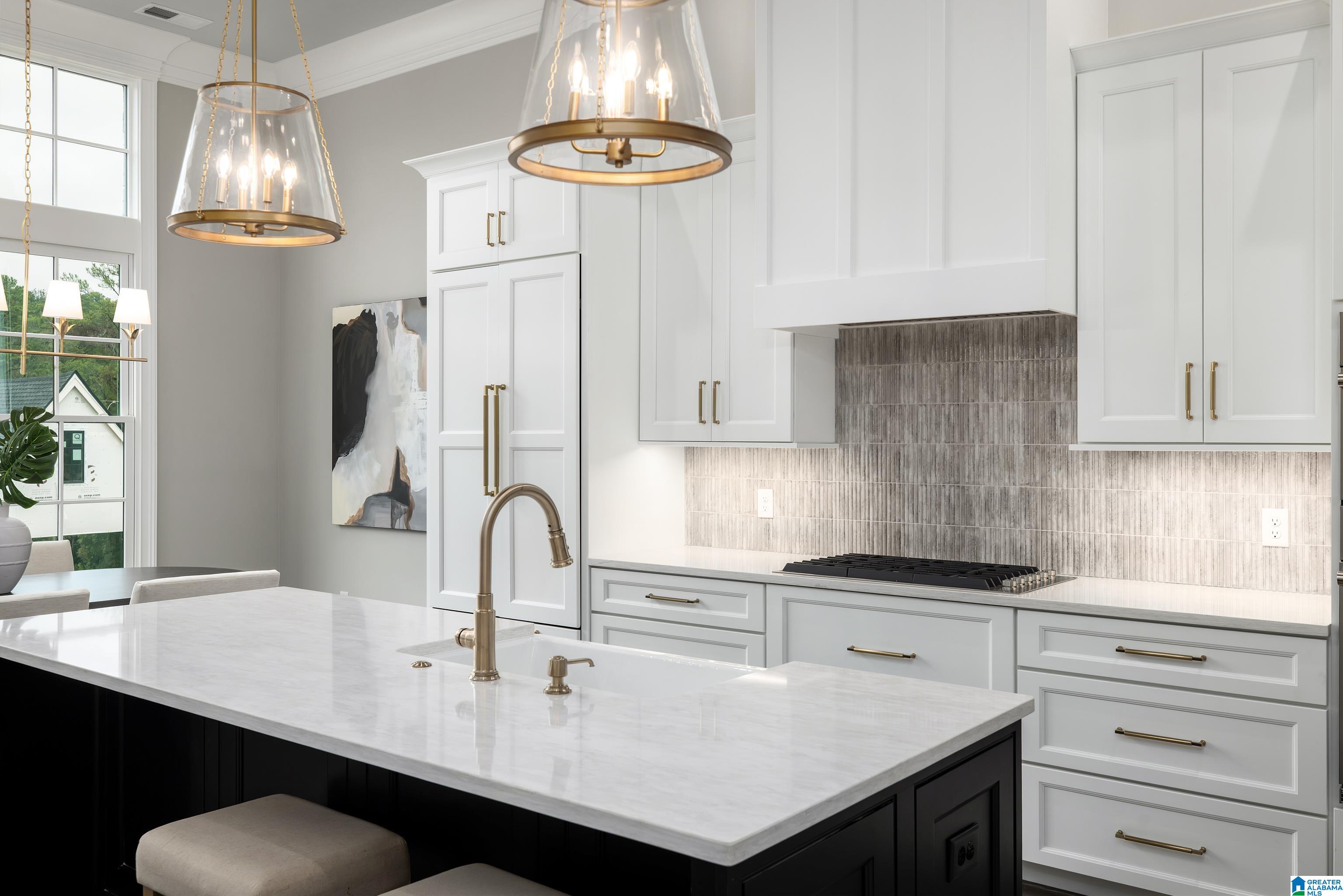 Bright kitchen with a dark island, white stone countertop, brass fixtures, and gray tile backsplash.