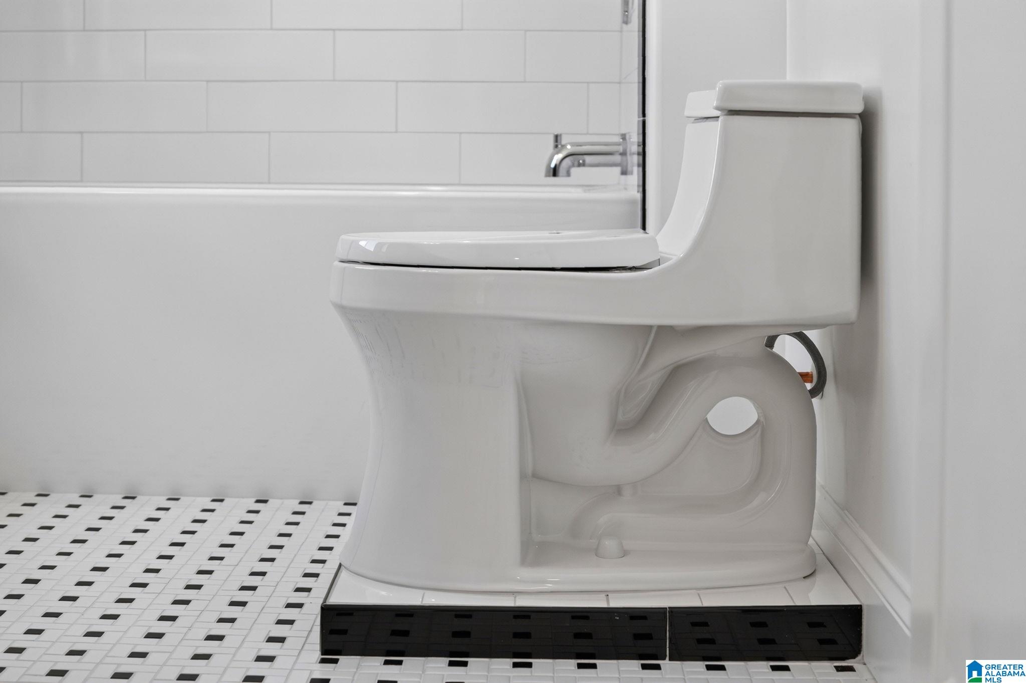 Bathroom toilet beside a tub, with white subway tile and a black-and-white mosaic floor.