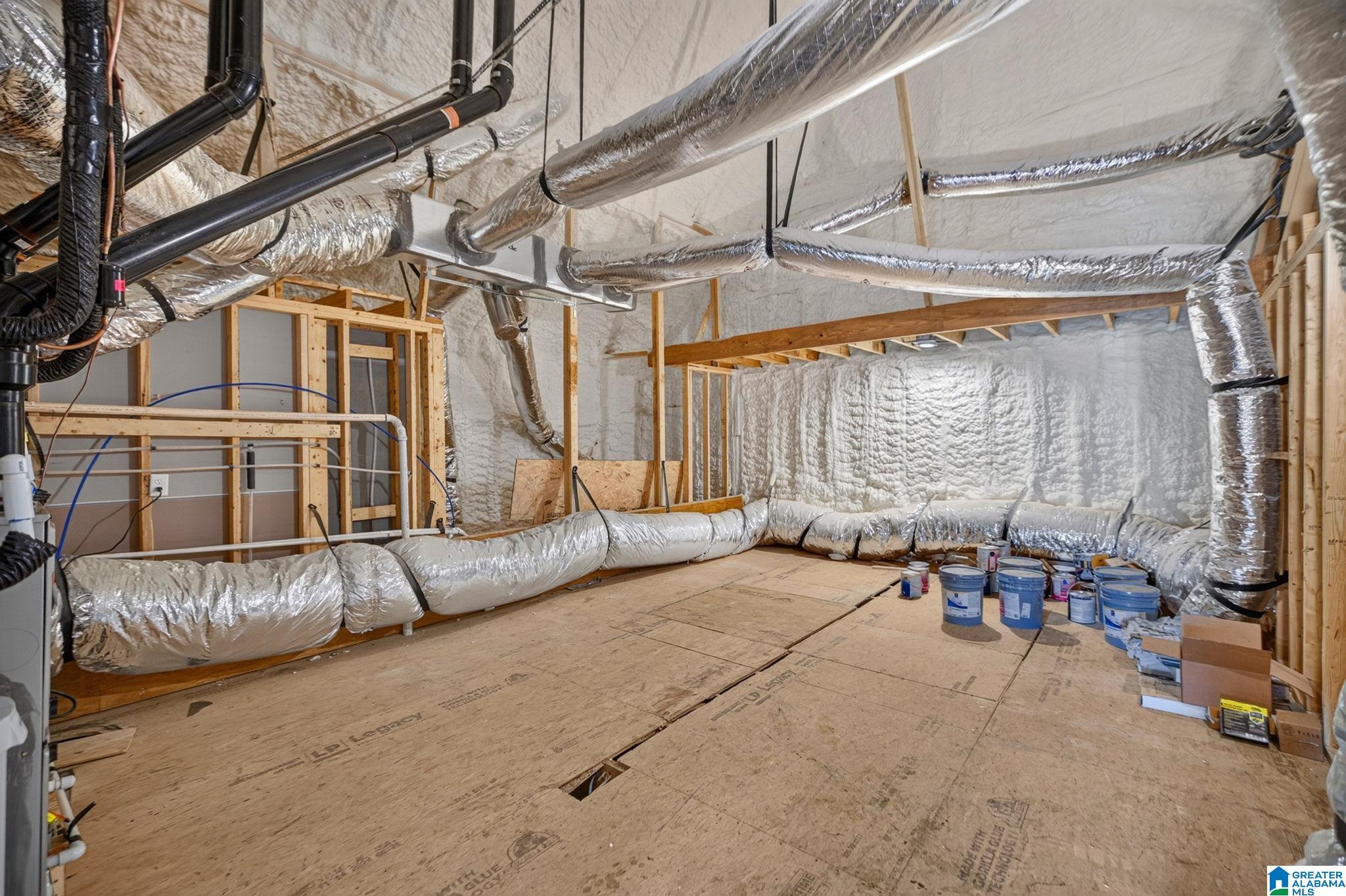 Unfinished attic with spray-foam insulation, exposed framing, and extensive silver HVAC ductwork.