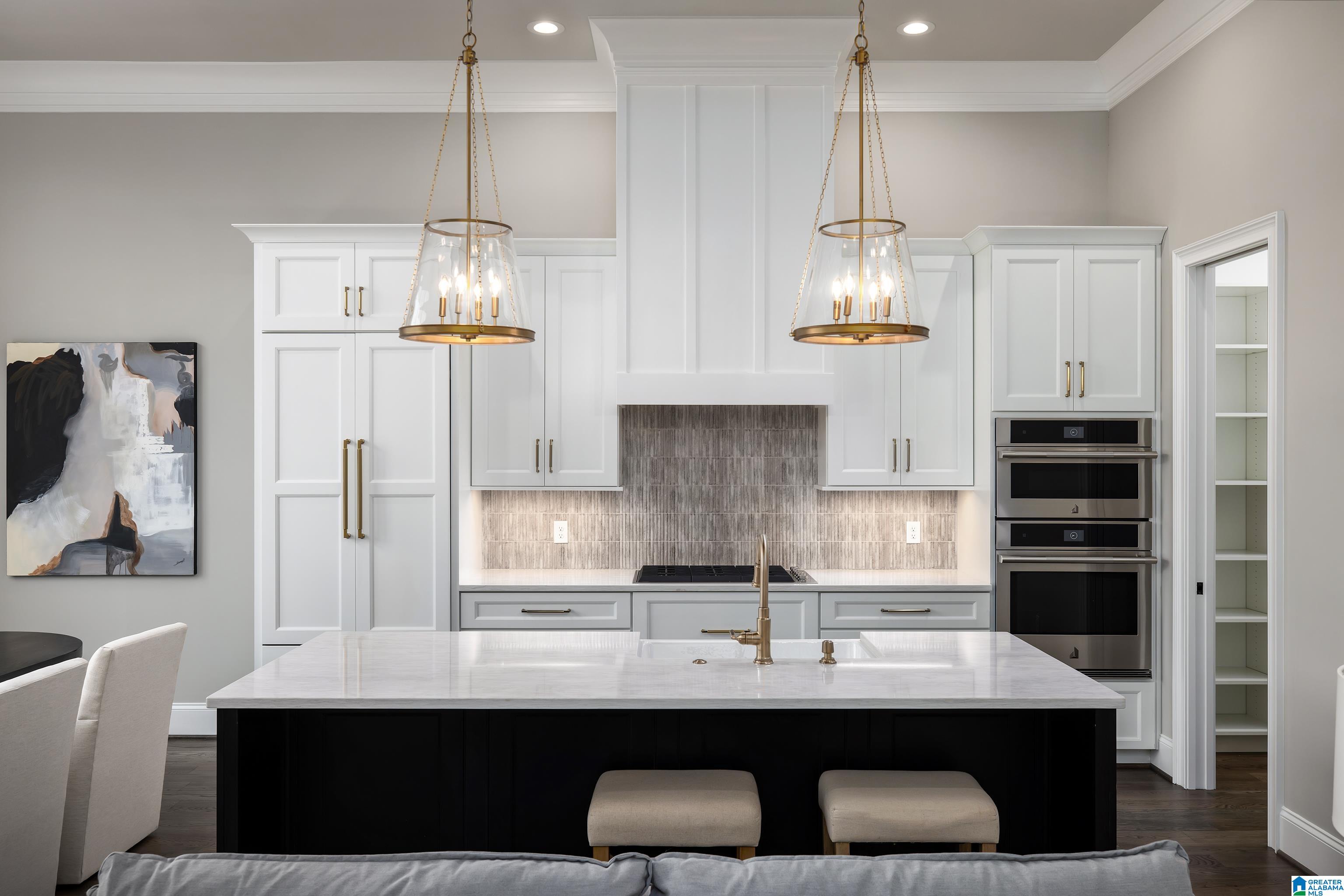 Kitchen with white shaker cabinets, a dark island, brass pendants, and a gray tile backsplash.