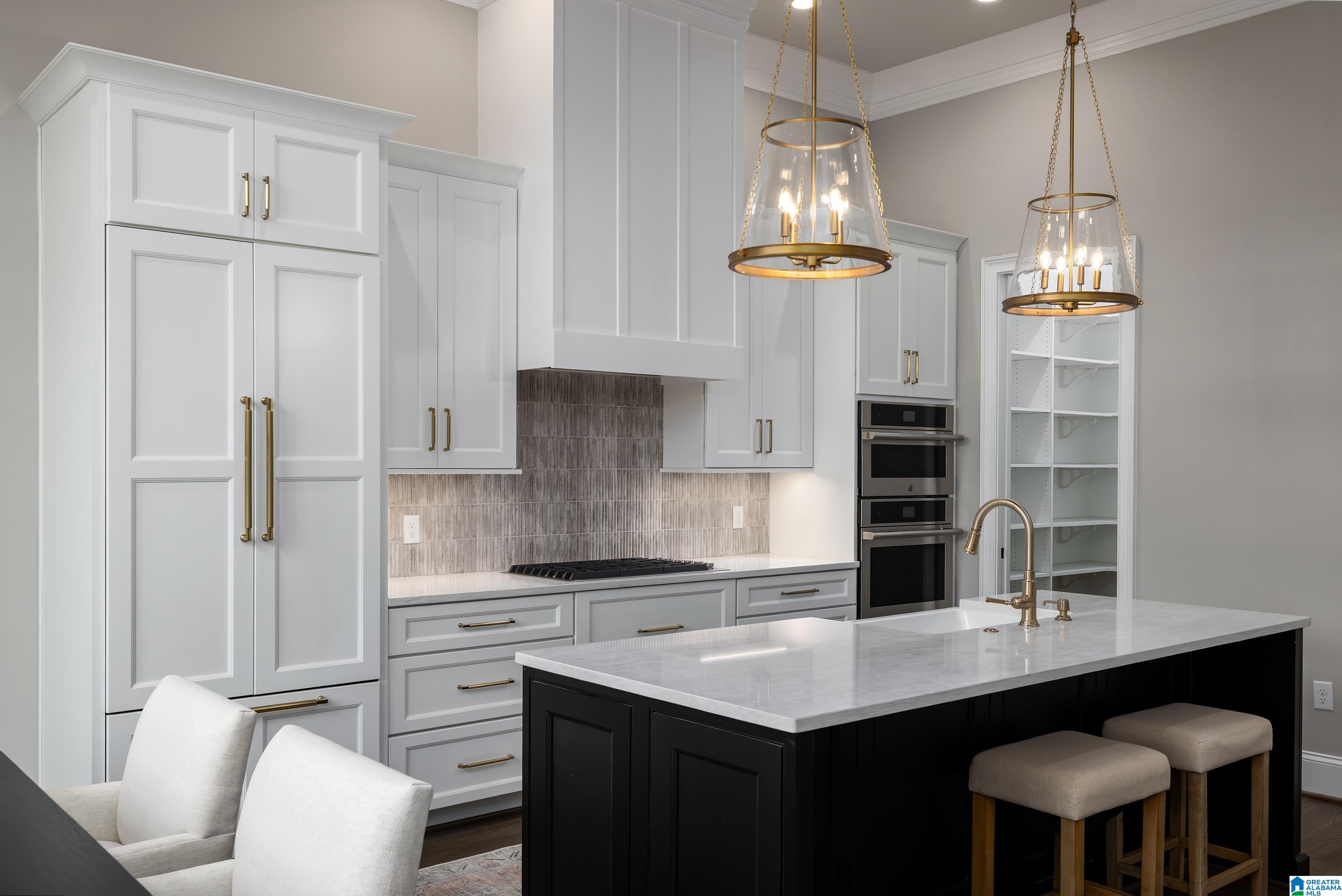 Bright kitchen with white cabinets, dark island, brass fixtures, and glass pendant lights.