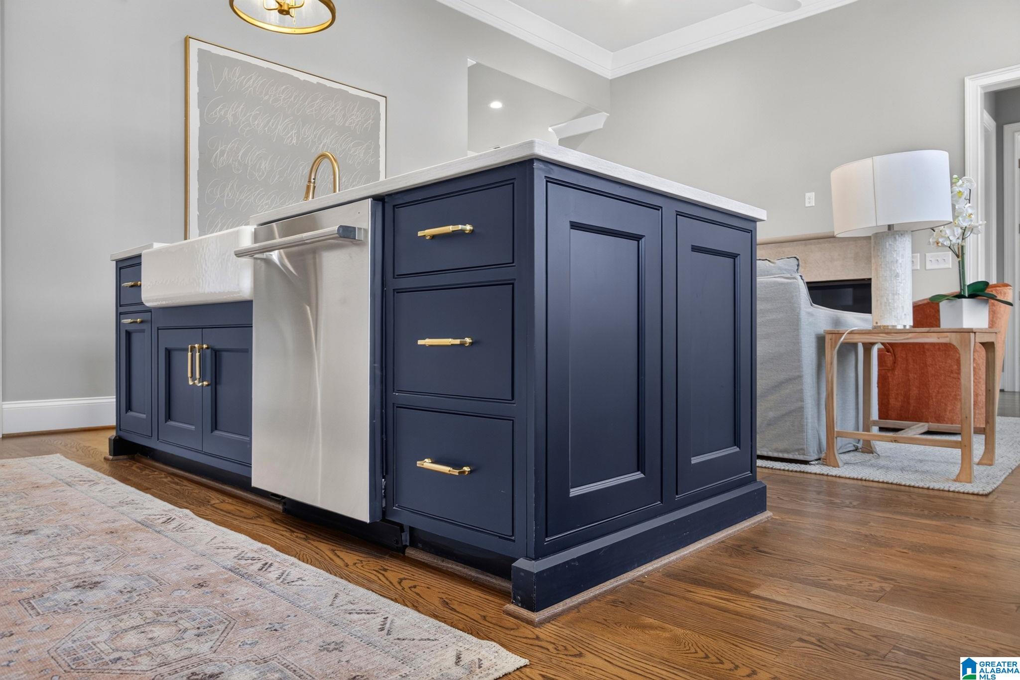 Navy kitchen island with gold hardware, white countertop, integrated sink, and stainless-steel dishwasher.