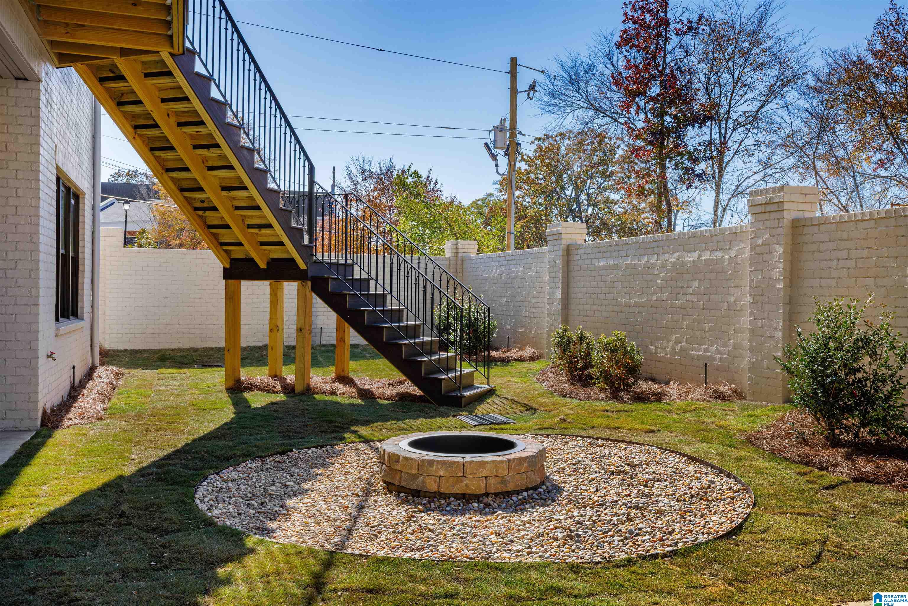 Backyard with an elevated deck staircase and circular stone fire pit in a pebble bed.
