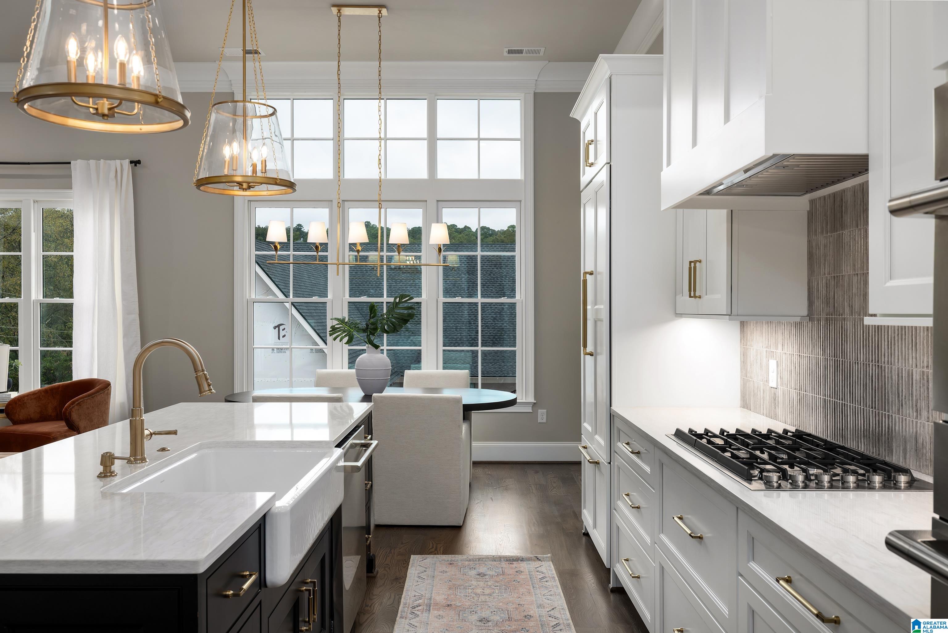 Bright kitchen with a marble-topped island, brass fixtures, gas range, and tall grid windows.
