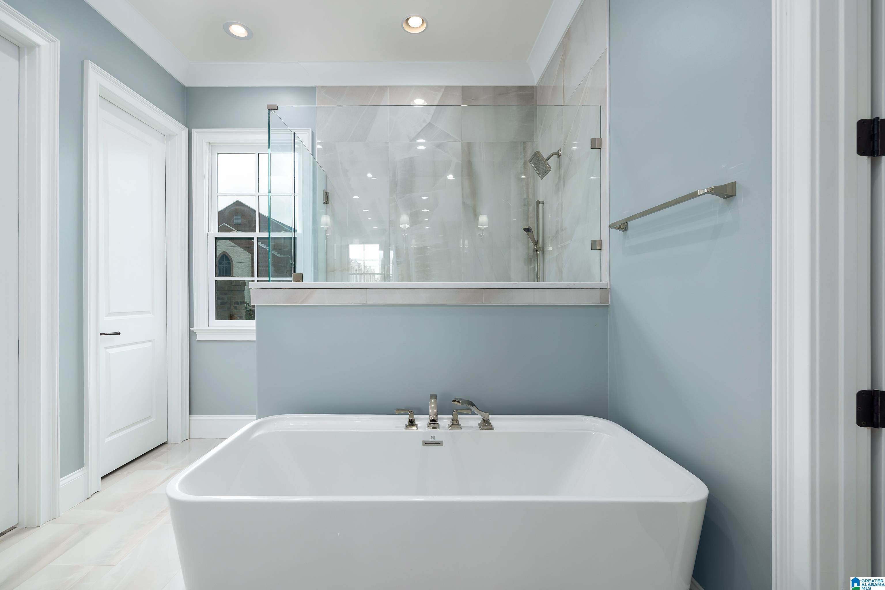Bathroom with a large freestanding tub, glass shower, and pale marble-look tile.