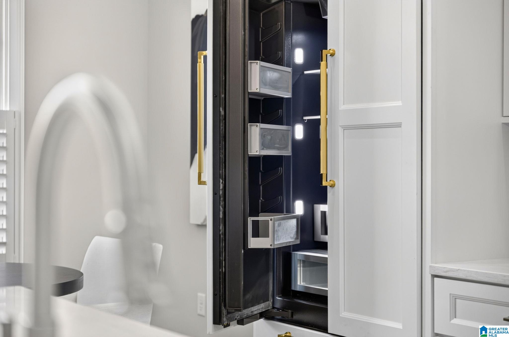 Open built-in refrigerator with dark shelving and brass handles in a white kitchen.