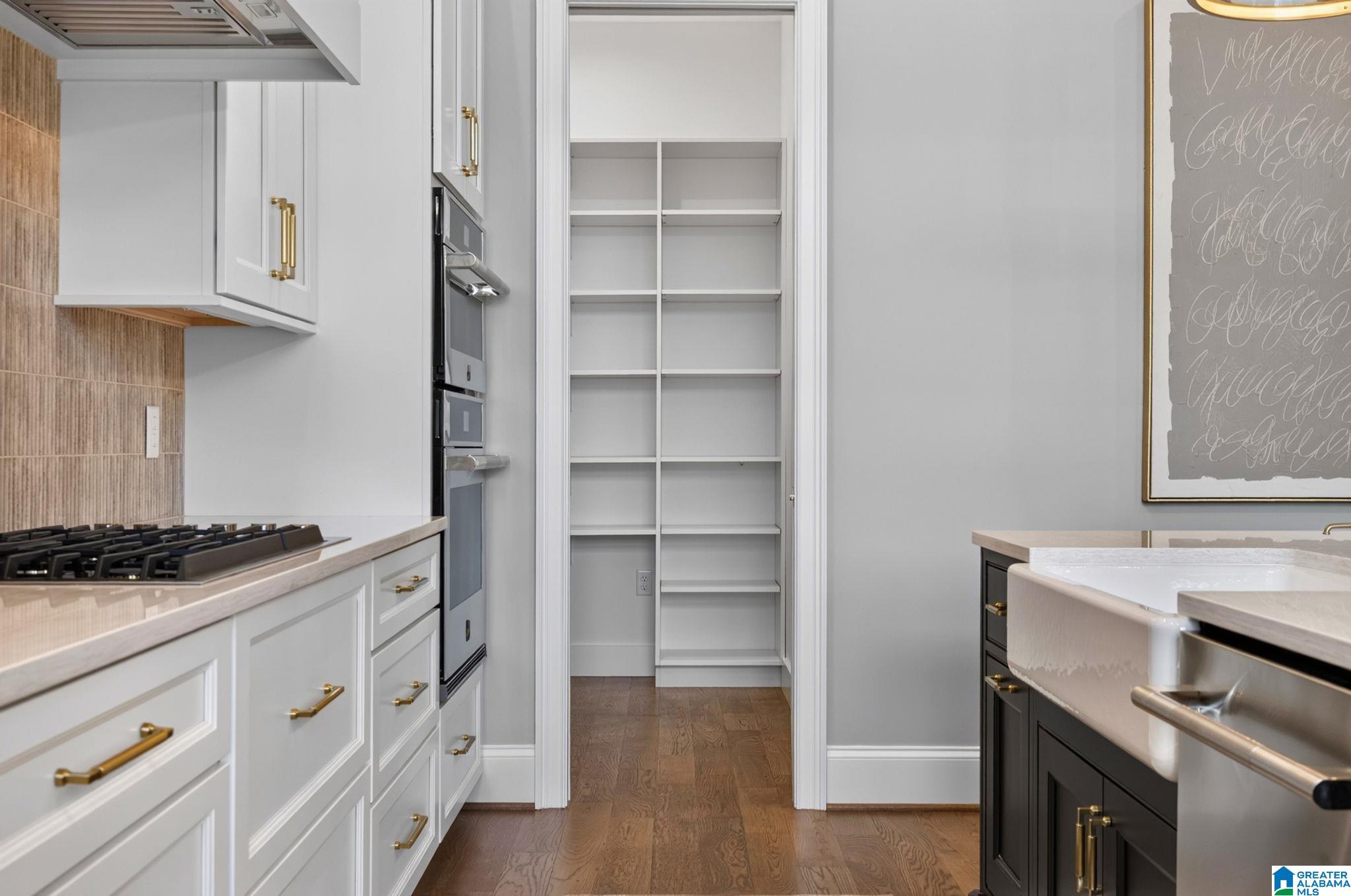 Kitchen with white cabinets, brass hardware, a farmhouse sink, and an open pantry with built-in shelves.