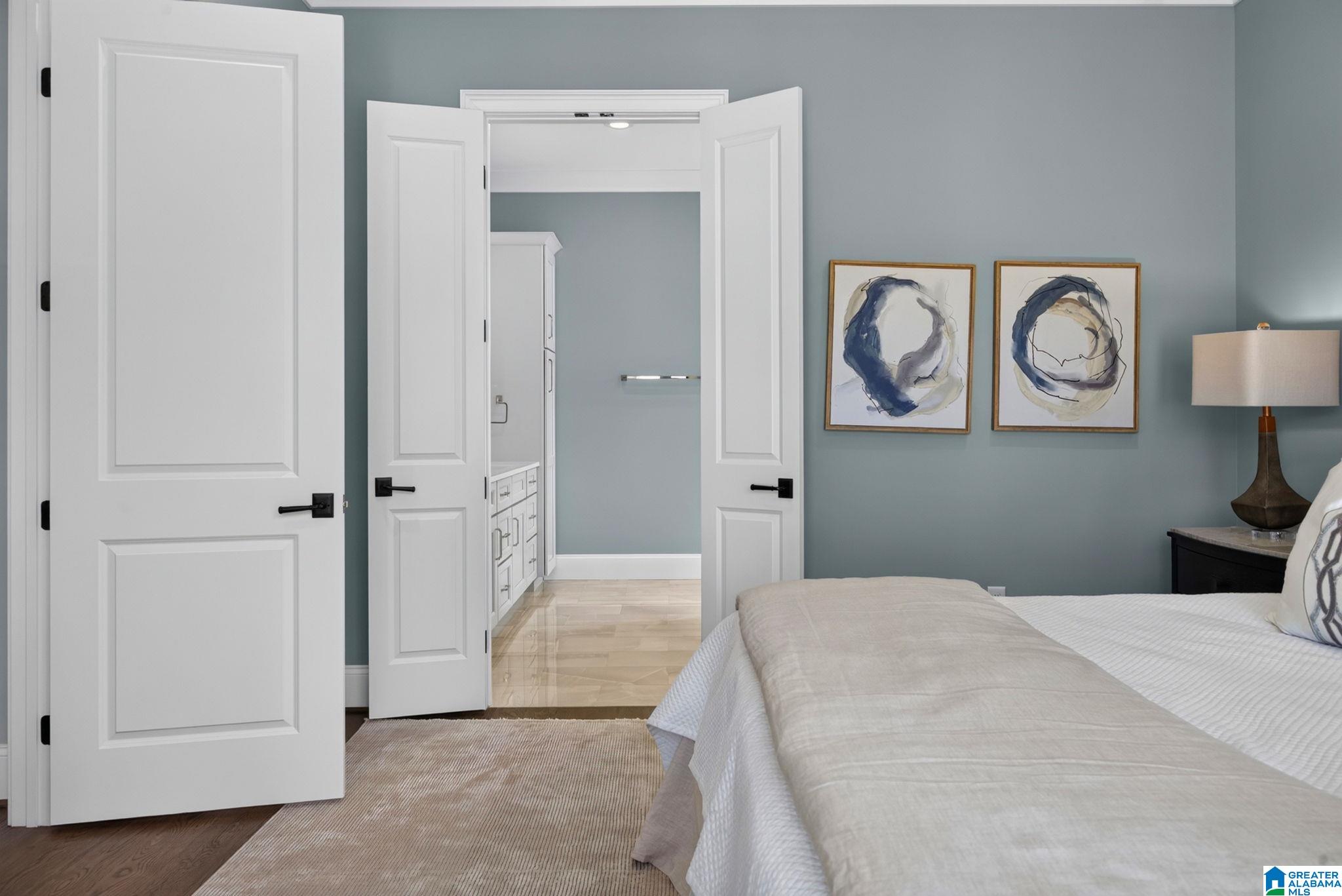 Bedroom with a white bed and open double doors to a bathroom with a white vanity.