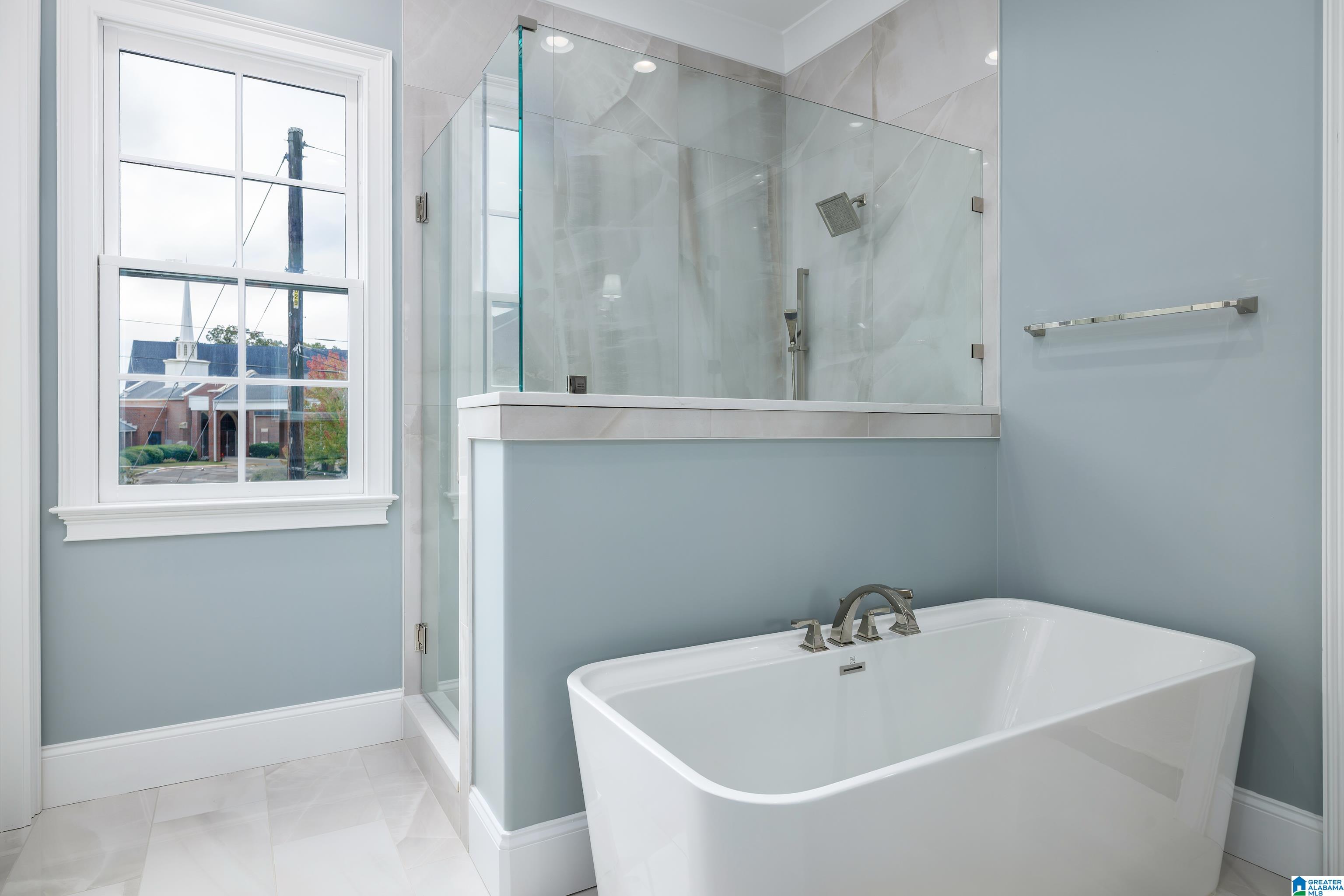 Bathroom with a freestanding soaking tub, glass shower, and large window.