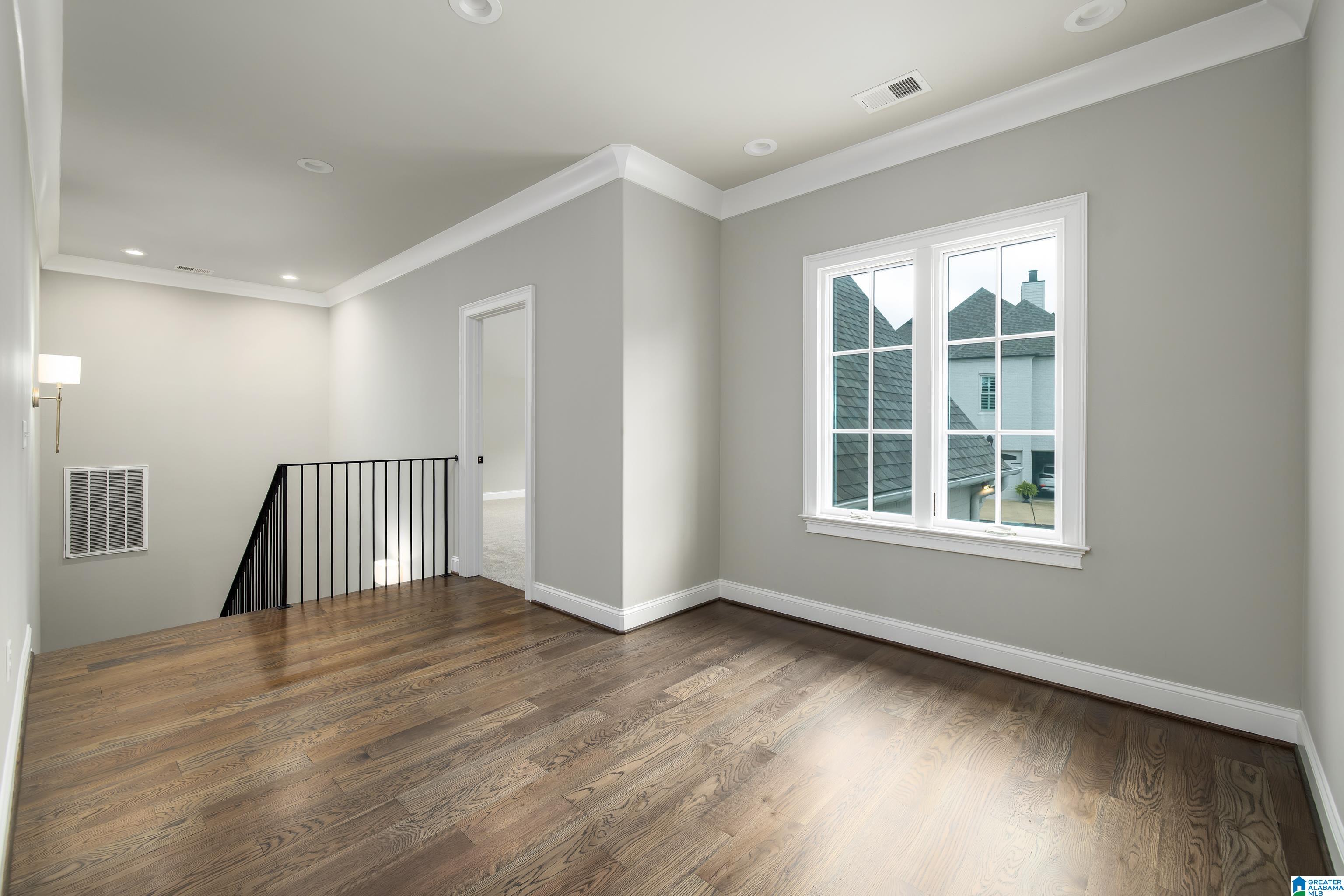 Empty upstairs landing with hardwood floors, a large window, and black metal stair railing.