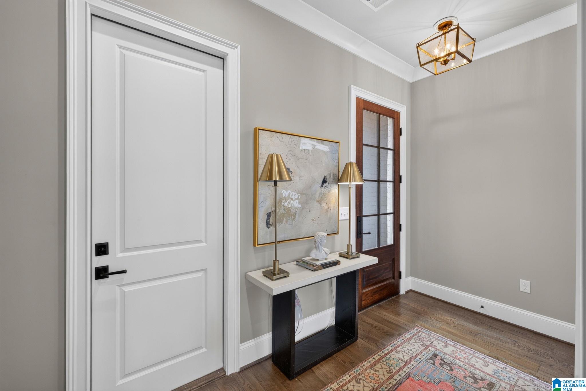Entryway with white paneled door, wood-and-glass door, and console table with brass lamps.